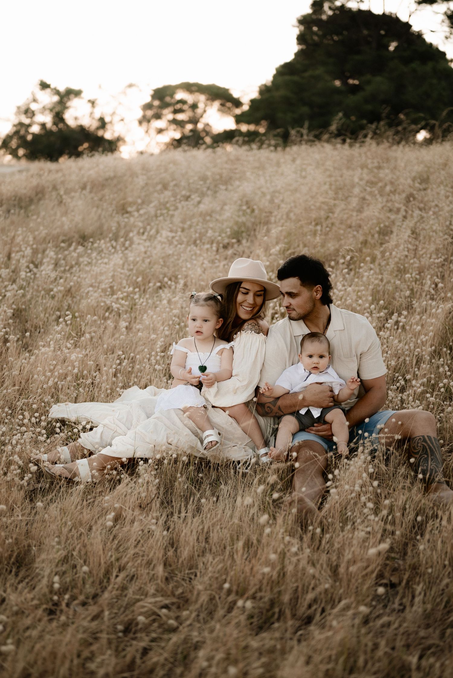 Family sits together in tall golden grass during sunset photoshoot.