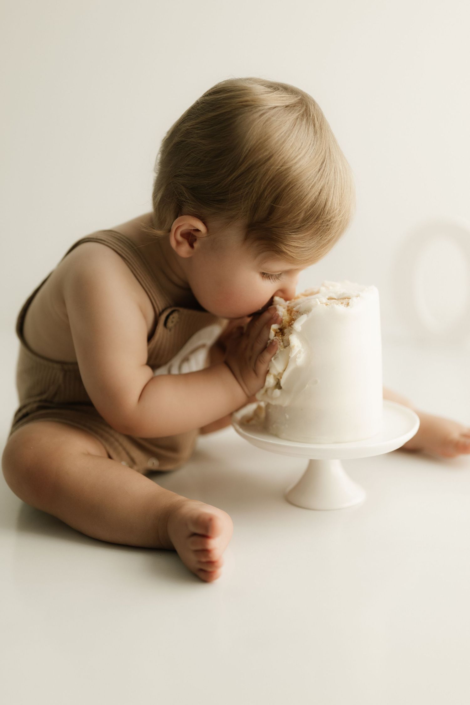 Baby in brown outfit eating white frosted cake.