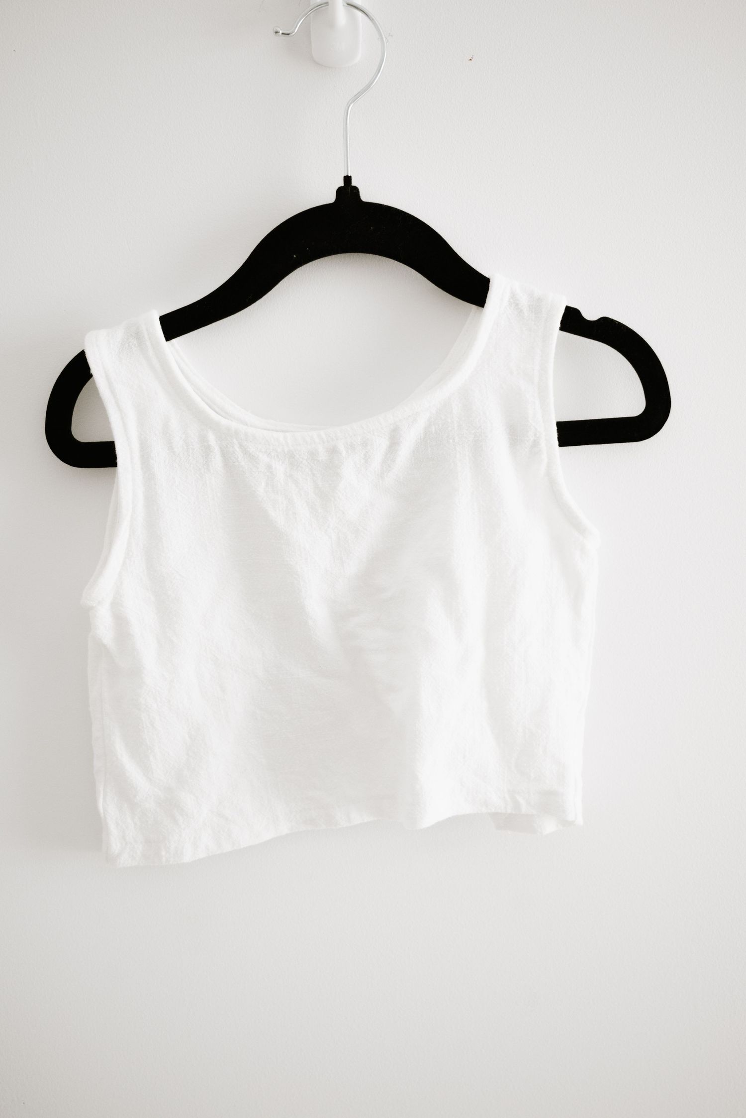 Simple white sleeveless crop top hanging on black velvet hanger.