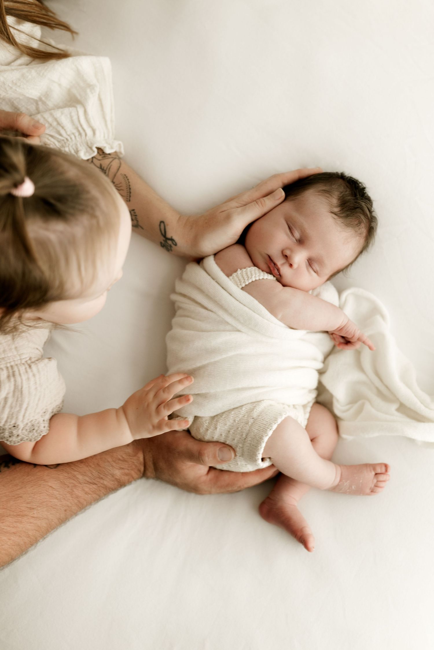 Peaceful sleeping newborn in white wrap with gentle hands nearby.