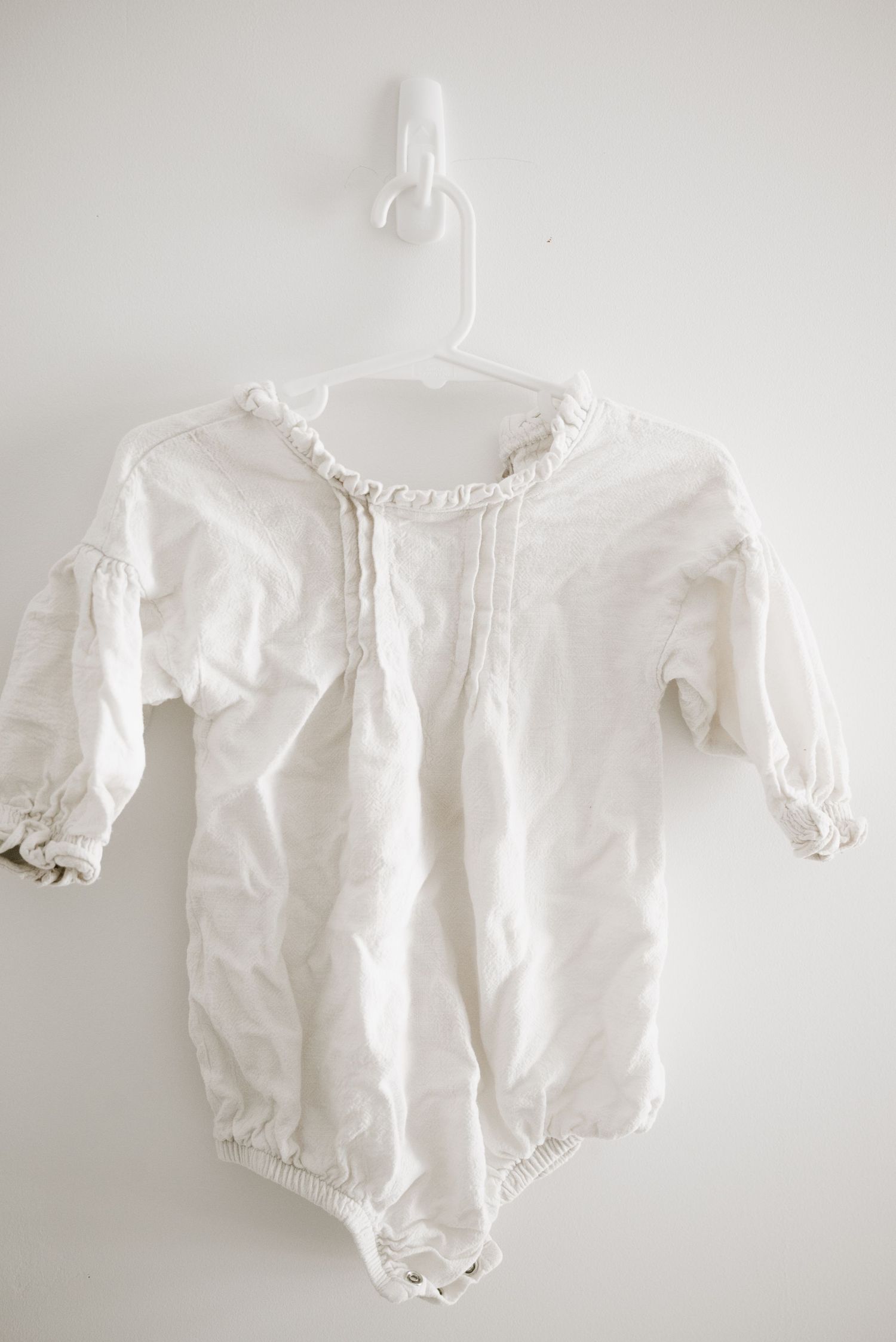A white cotton baby romper with ruffled neckline and gathered sleeves.