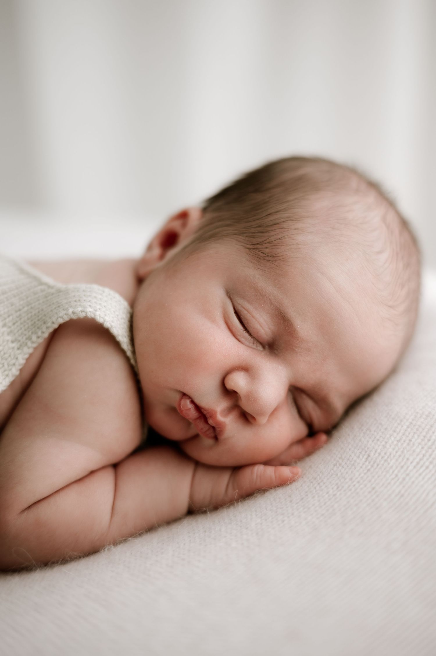 Sweet peaceful sleeping newborn baby resting on soft white fabric in gentle natural light during photography session.