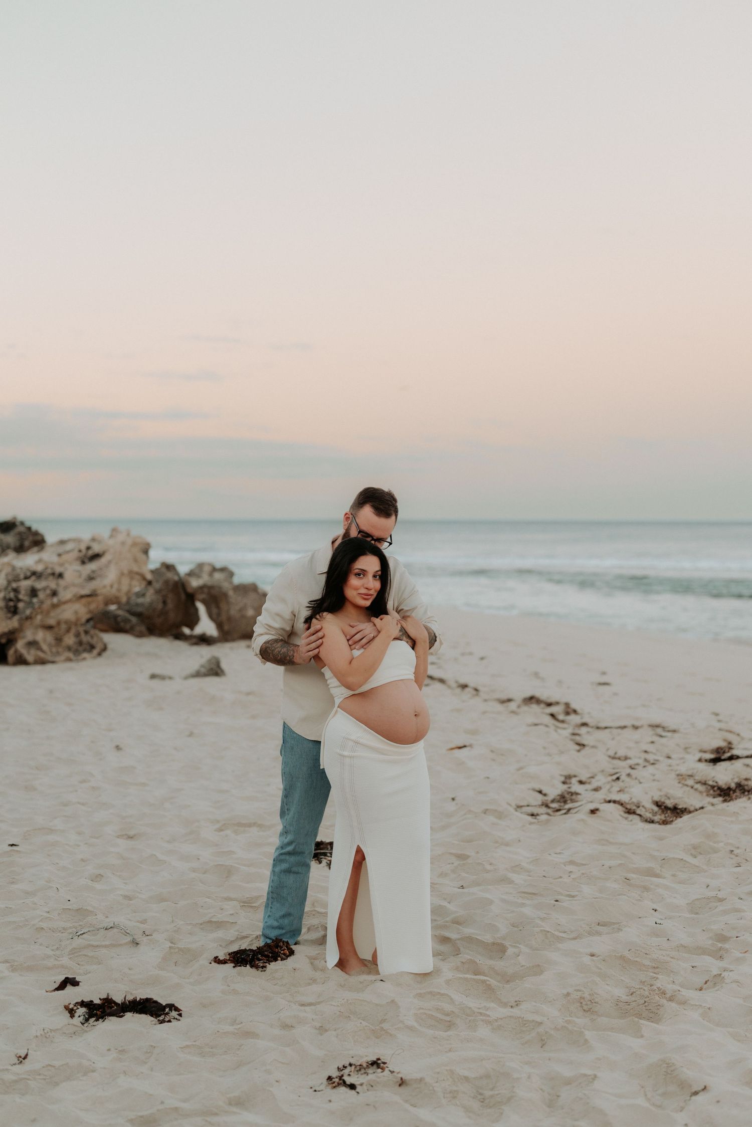 Intimate beach portrait of couple embracing on sandy shore at sunset.