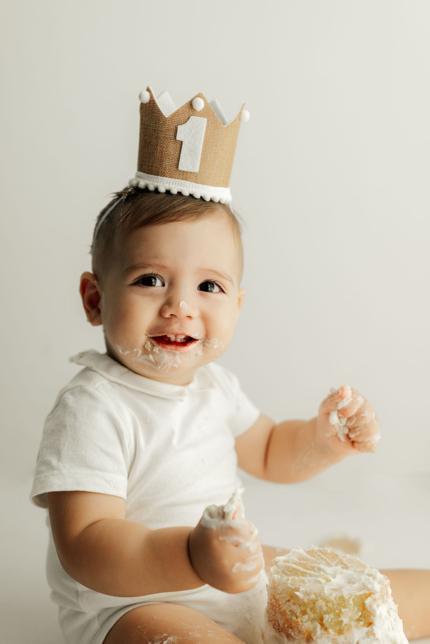 Baby wearing gold paper crown smiling with cake smeared on face.
