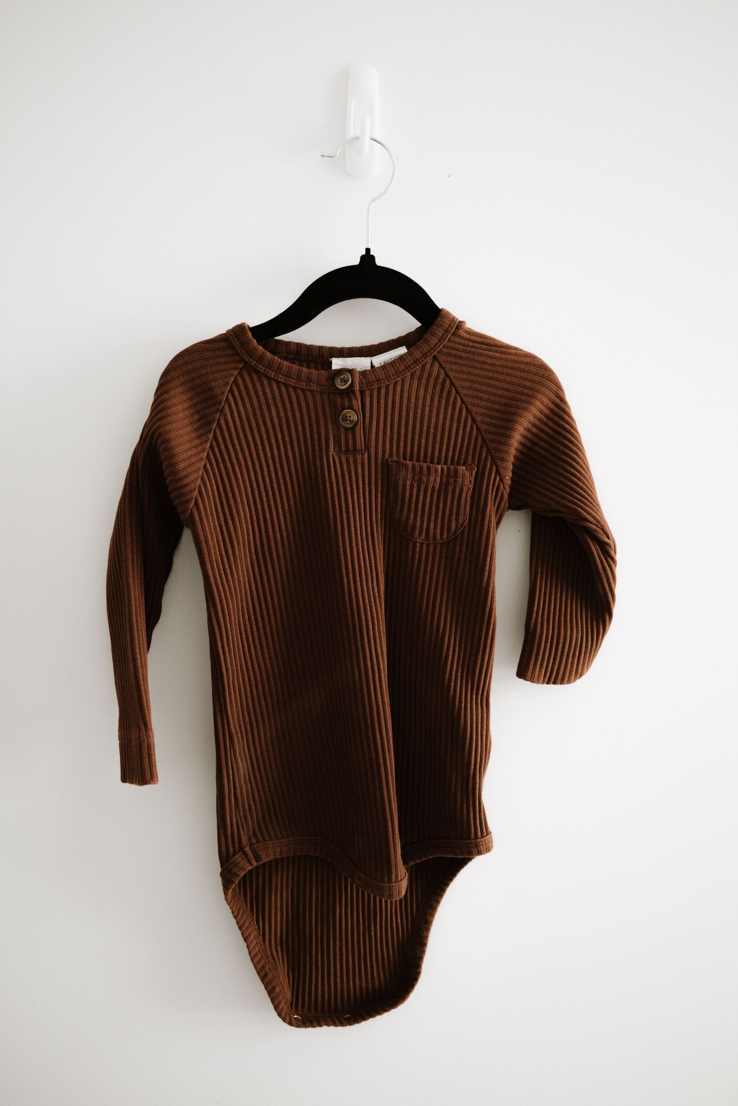 Brown ribbed knit henley bodysuit with long sleeves on black hanger.