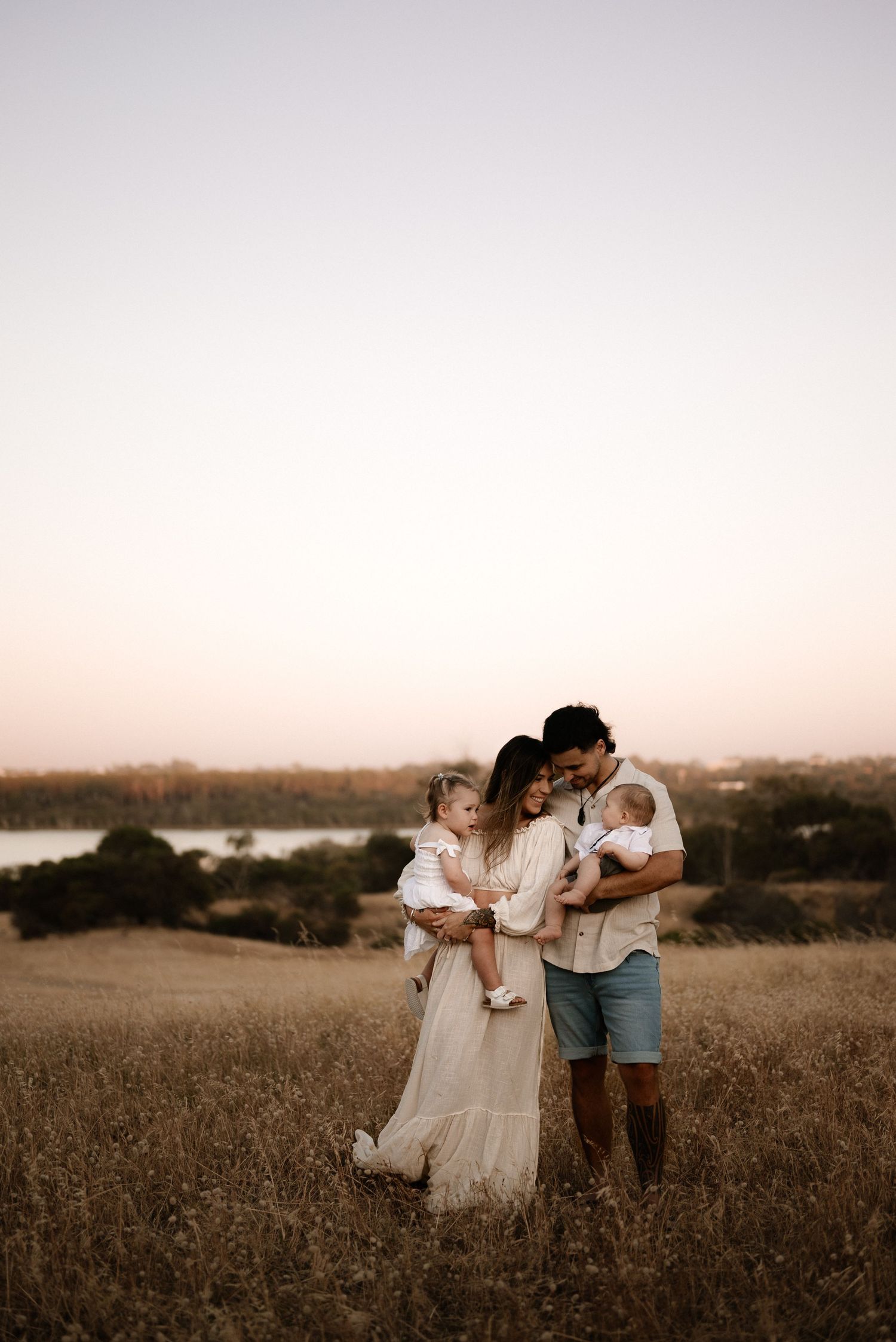 Family enjoying a tender moment together at sunset in a golden field overlooking water.