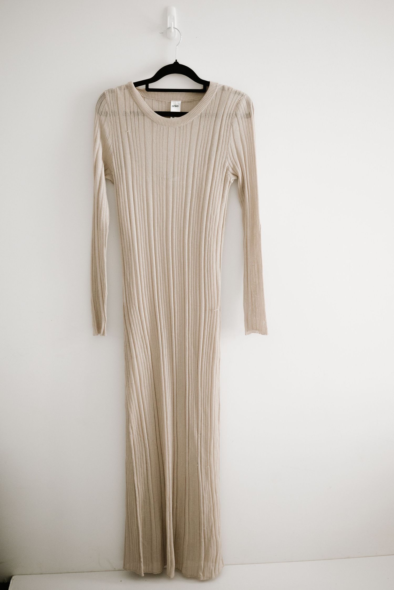 A sleek beige ribbed knit maxi dress with long sleeves hanging on a black hanger.