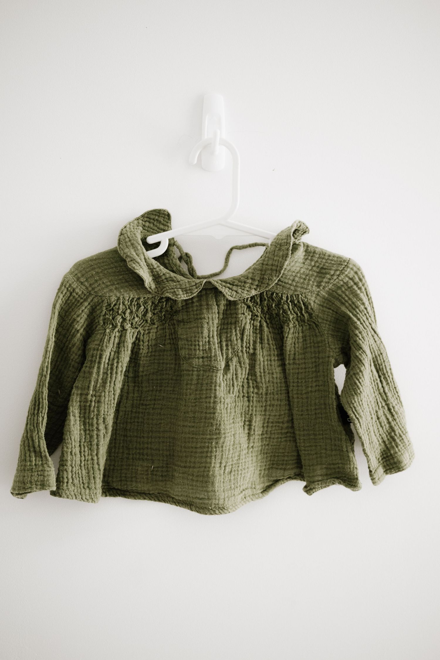 Sage green textured cotton blouse with gathered neckline and long sleeves hanging on display.