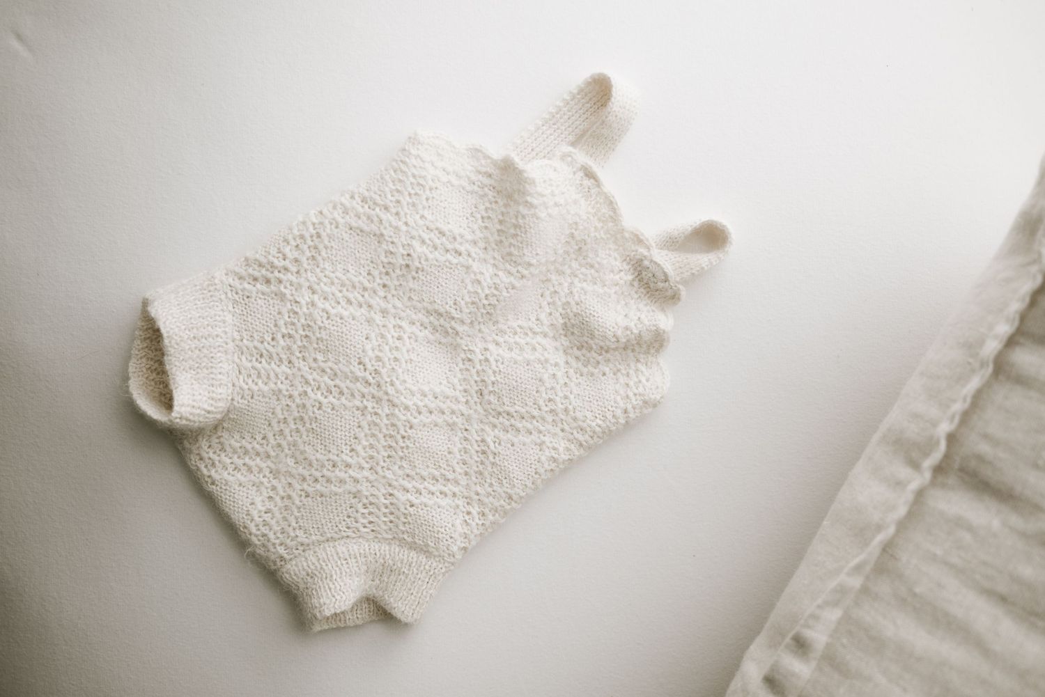 White textured knit baby romper laid flat on white surface.
