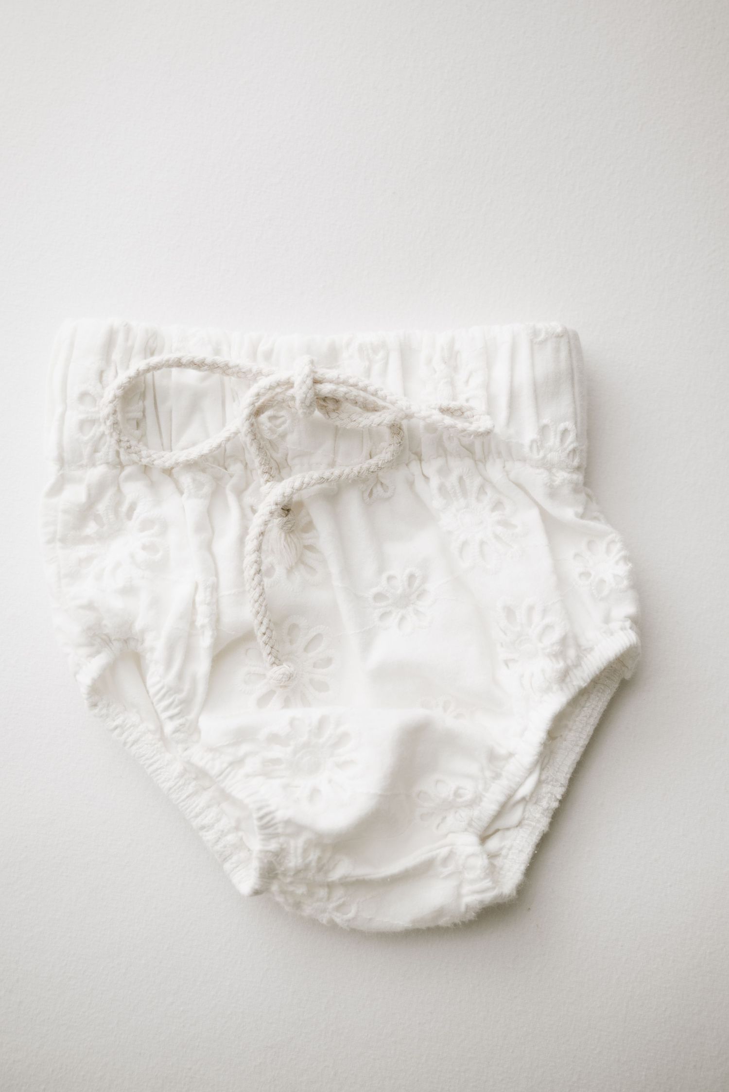 White cotton baby diaper cover with drawstring waist and ruffled edges.
