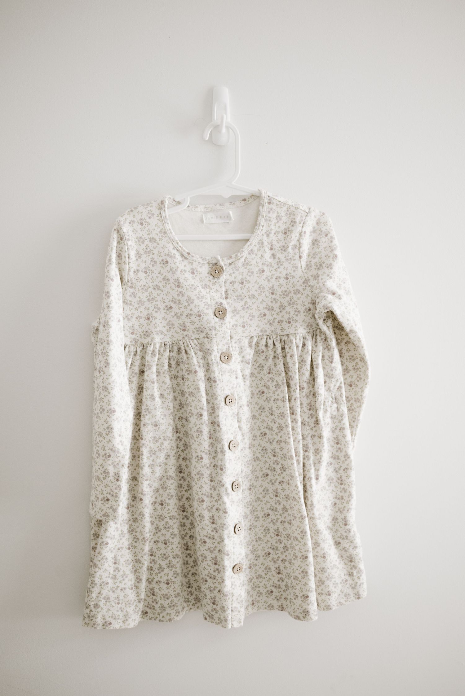 White button-down dress with delicate floral print and long sleeves on white hanger.