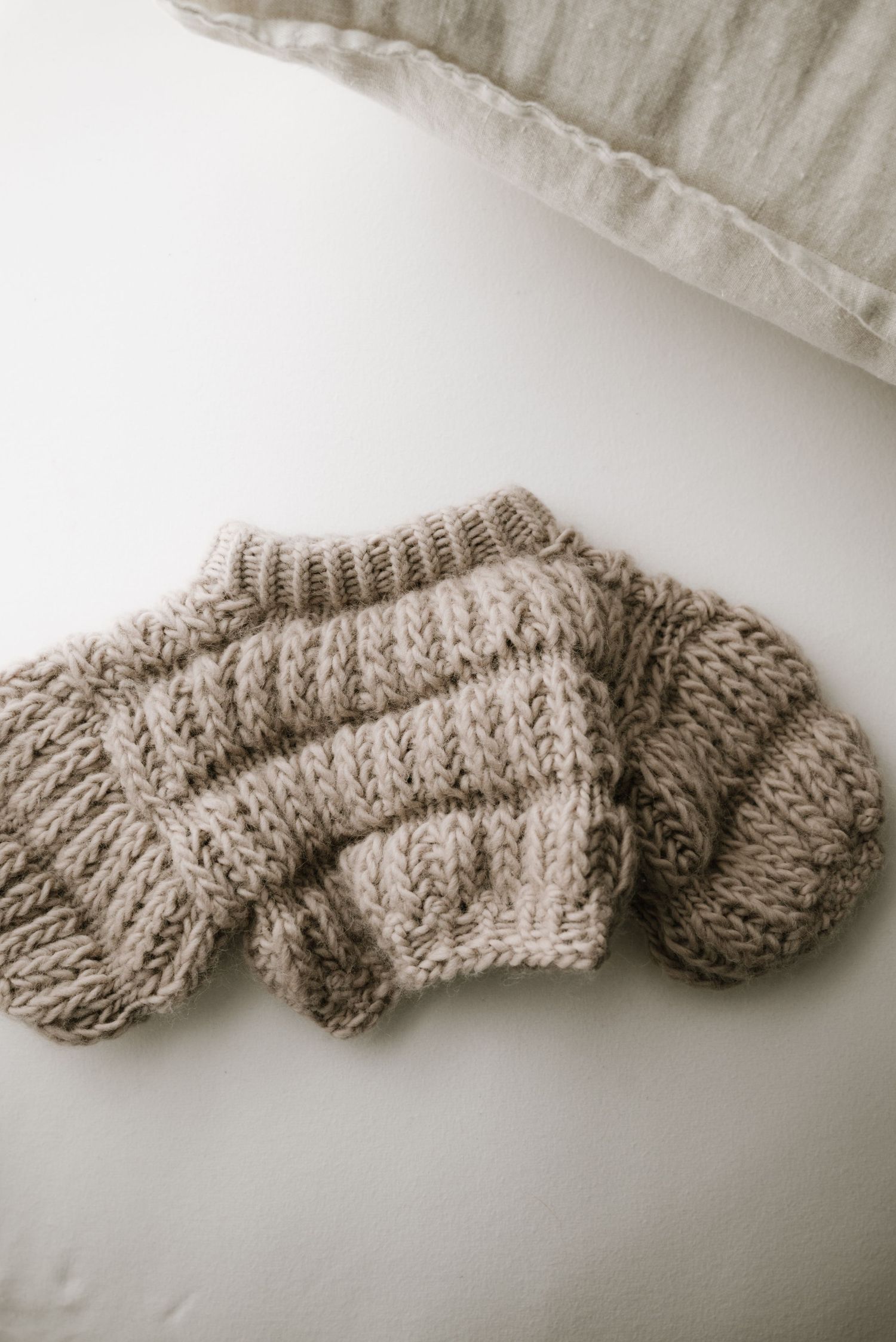 Gray chunky knit baby sweater laid flat on white bedding.