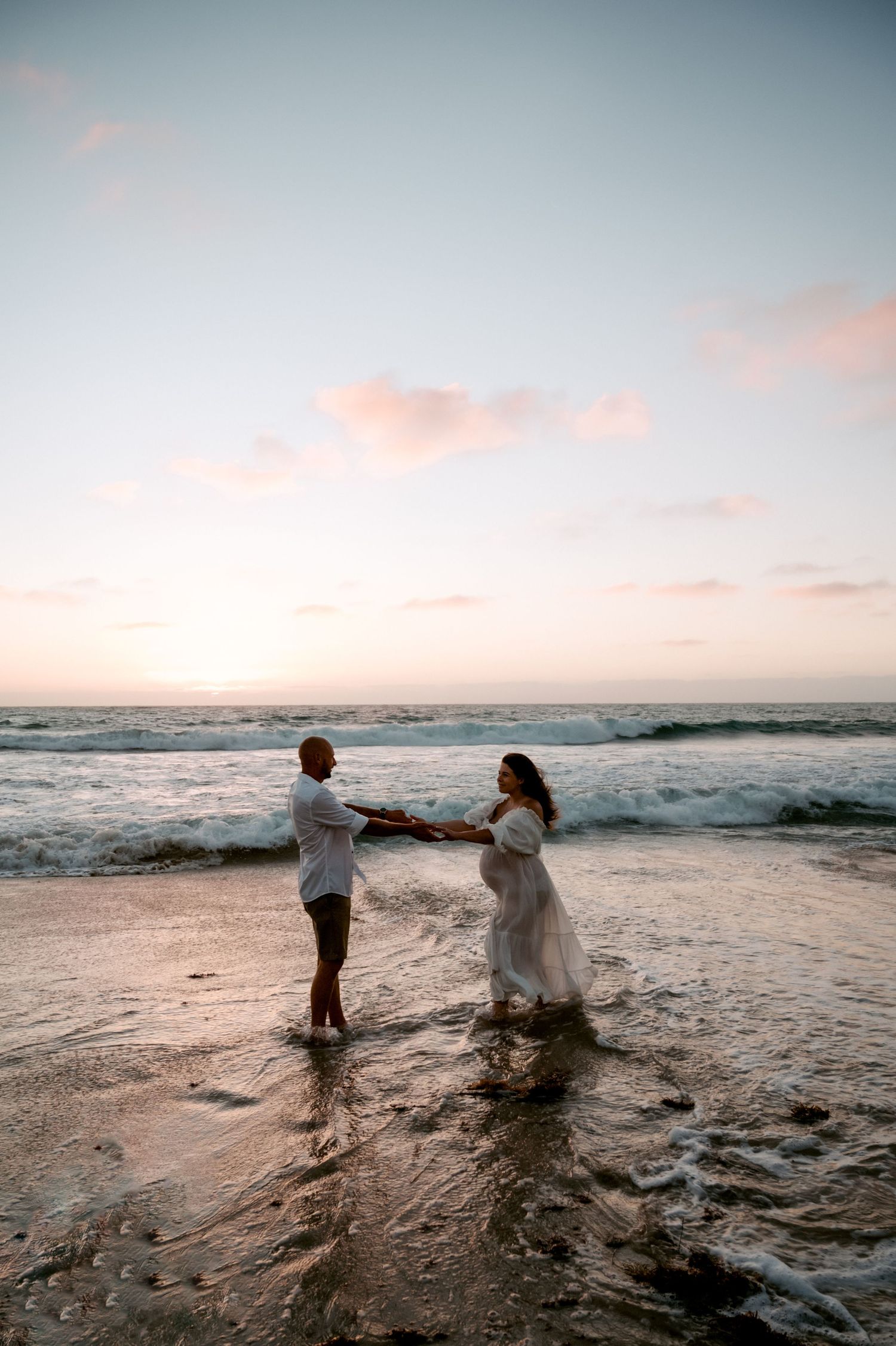 Two people dance together on a sunset beach as ocean waves crash against the shore at dusk.