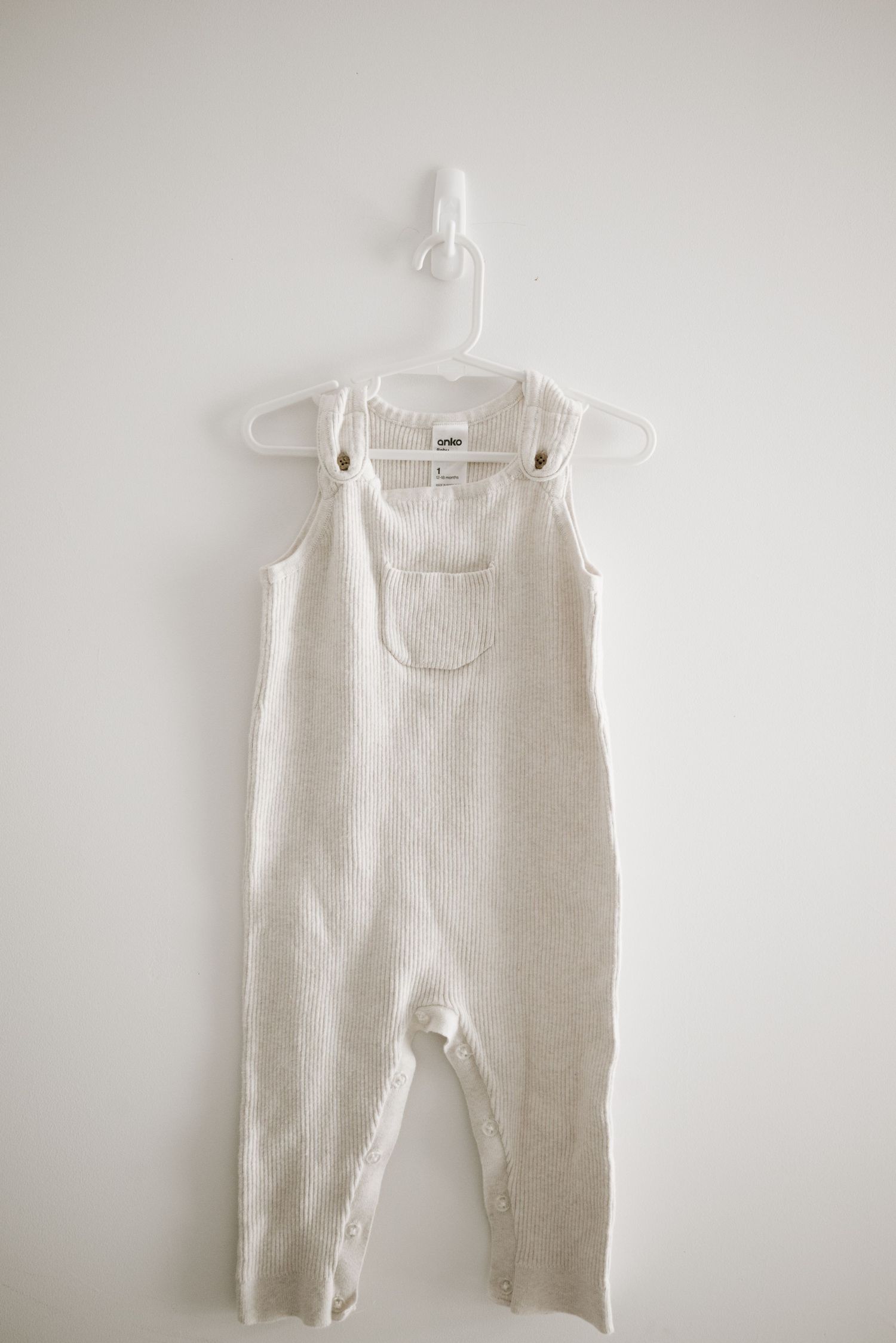 White ribbed cotton sleeveless romper hanging on plastic hanger against light background.