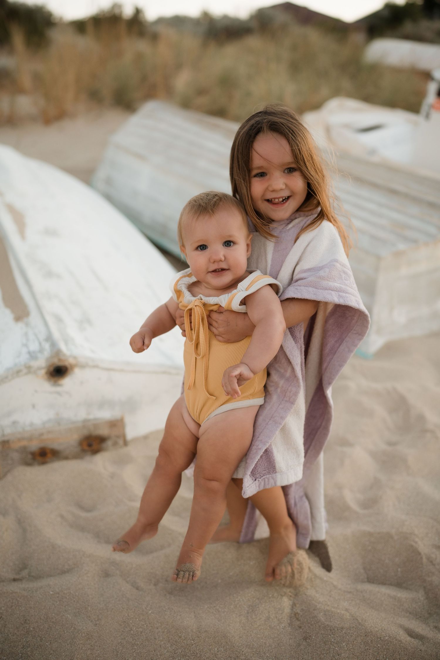 Sweet family beach portrait with baby in yellow romper and matching smiles.