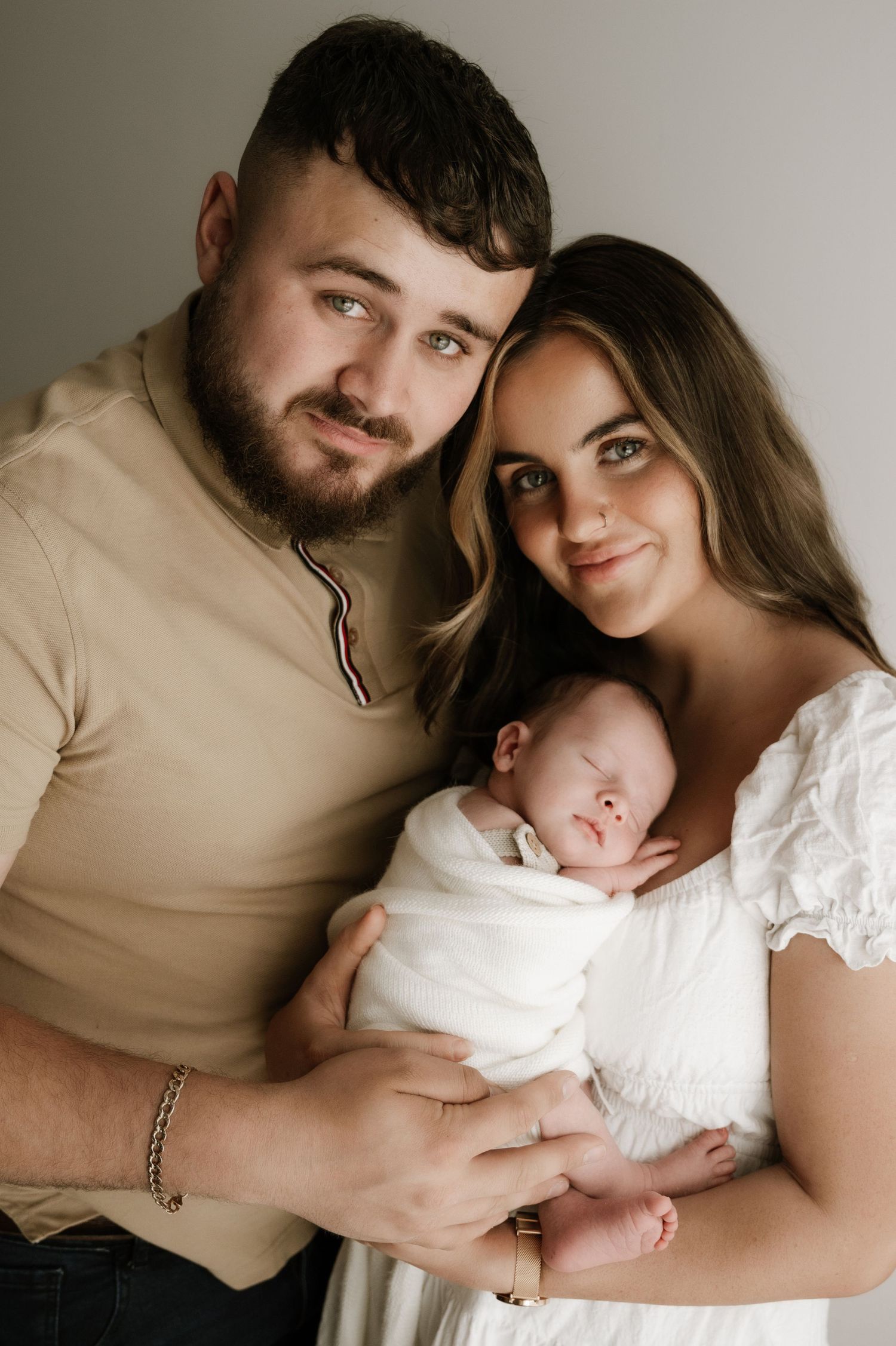 Young family poses together with their newborn baby in a studio setting.