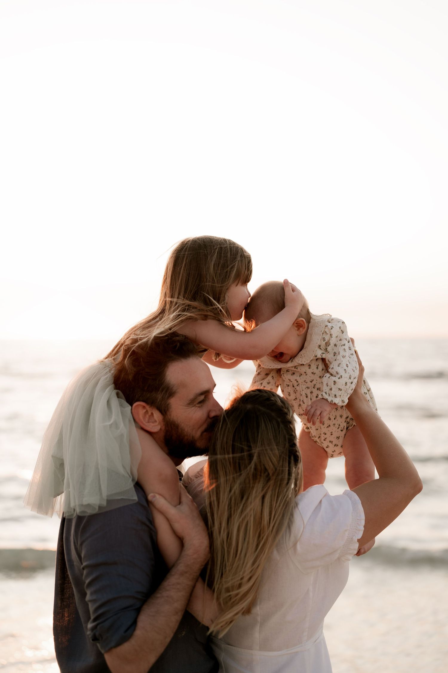 Family shares loving embrace on beach at sunset with waves in background.