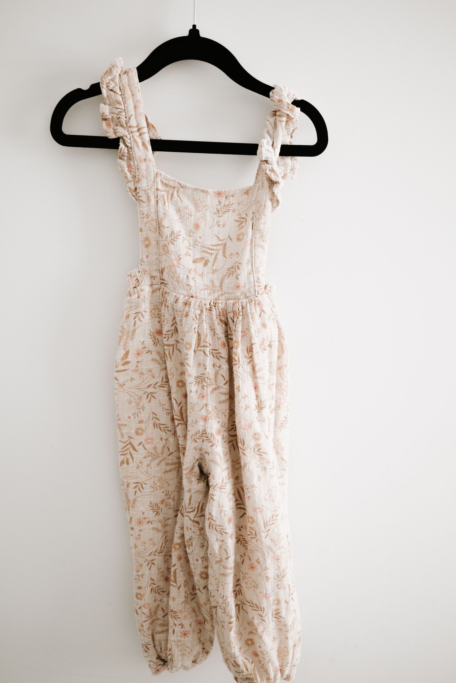 Beige floral print romper with ruffled straps and gathered waist hanging on black hanger.