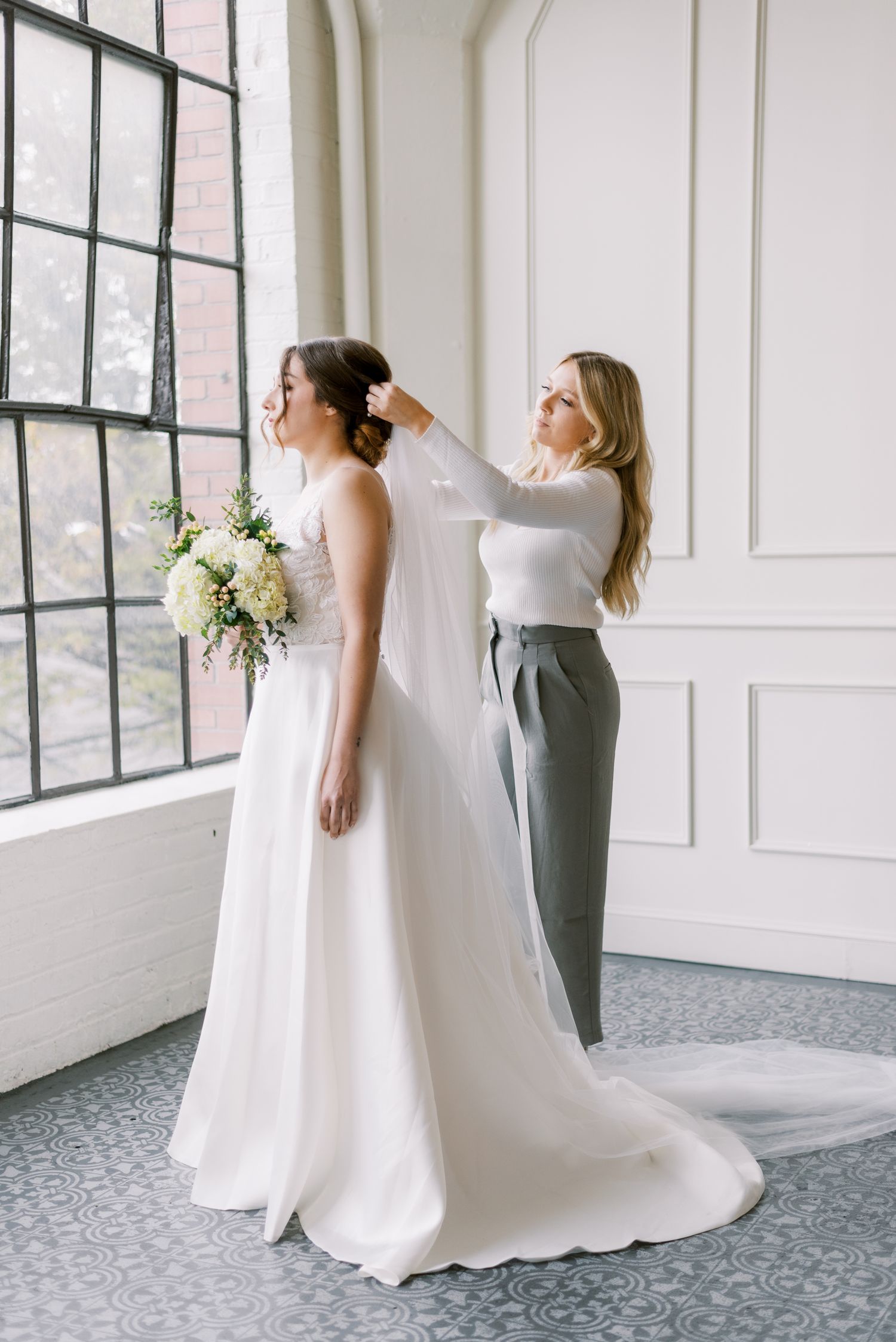Helper assists with final touches on a wedding dress in an elegant bright room.