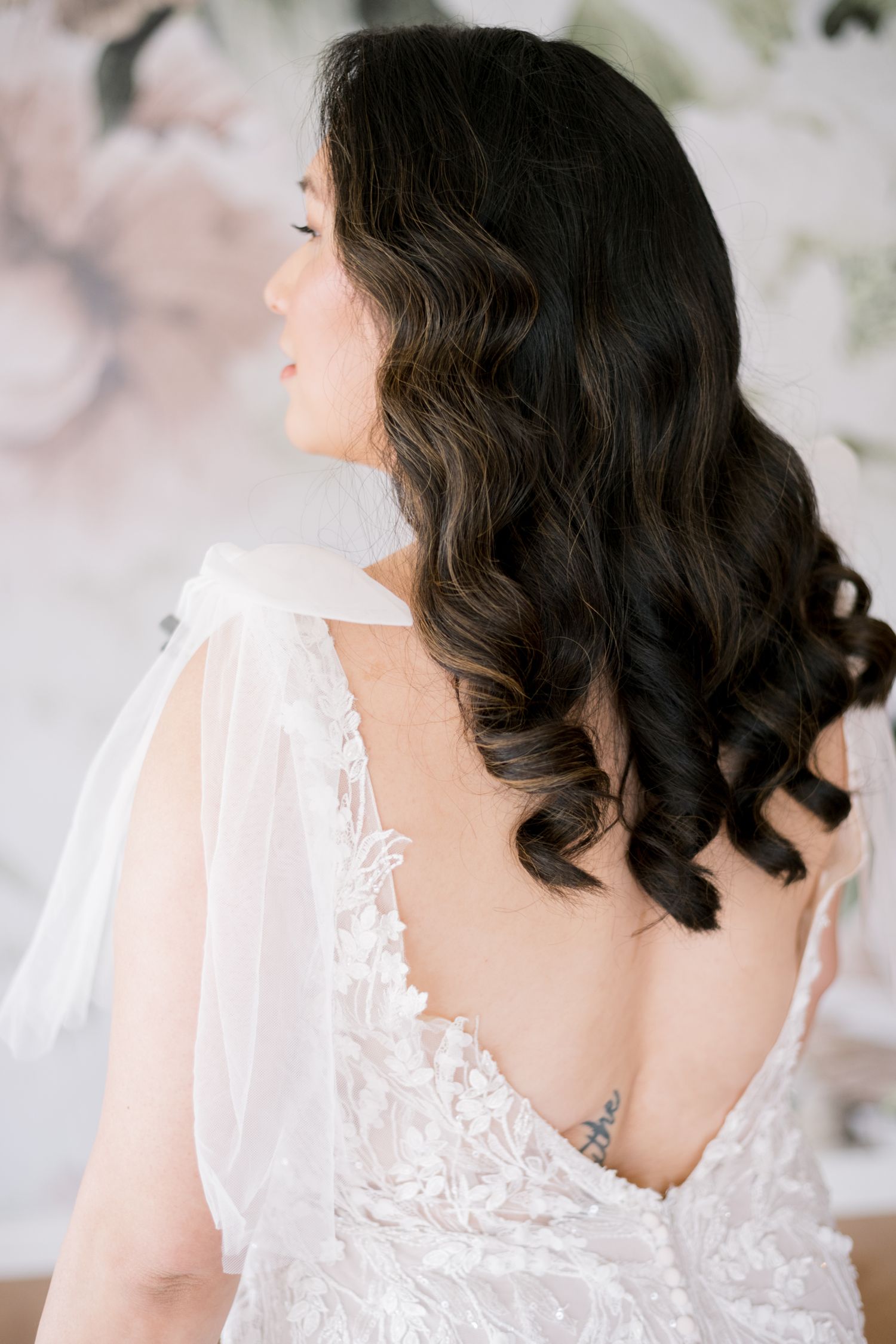 Back view of bride showing detailed lace dress and flowing dark curls.