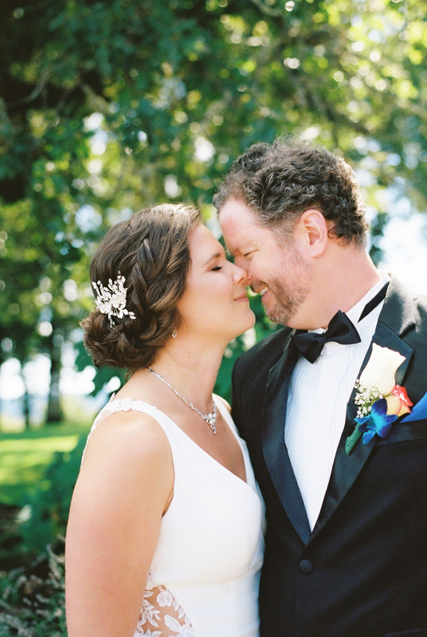 A joyful wedding portrait capturing a tender moment between newlyweds under green trees.