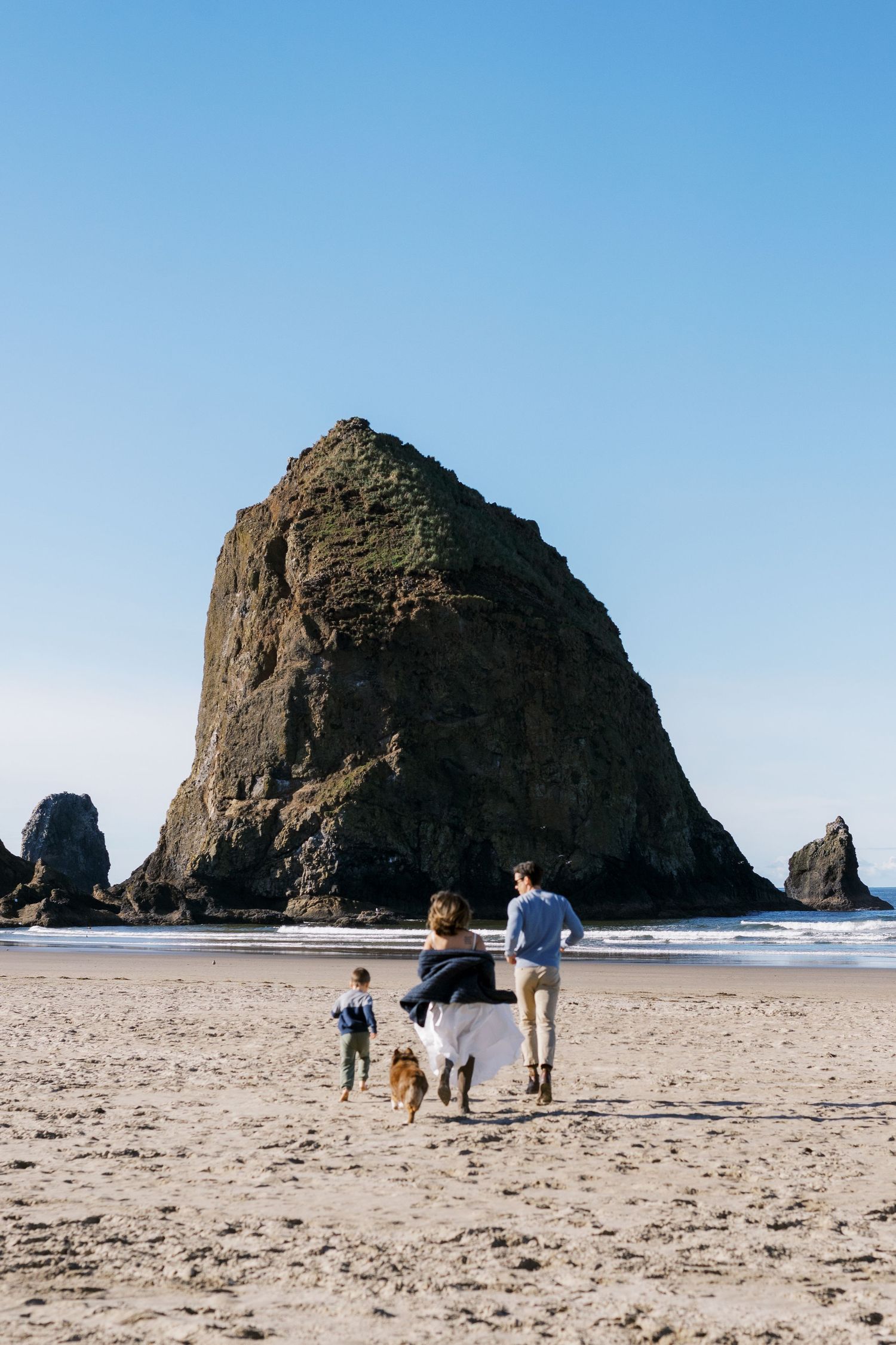 Family walking with their dog on Cannon Beach with the iconic Haystack Rock formation towering in the background.