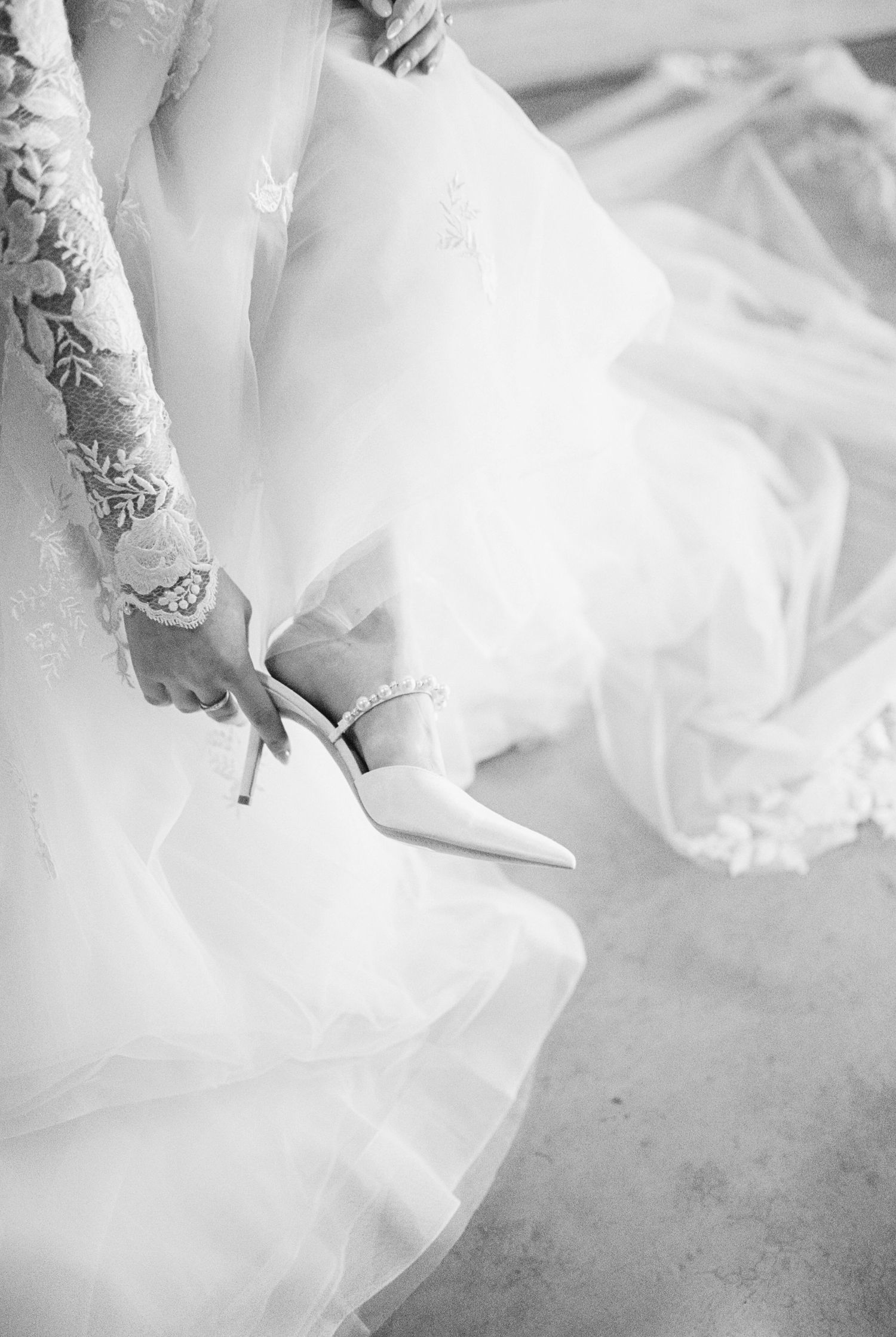 Close-up of lace wedding dress details and bridal shoes in black and white.