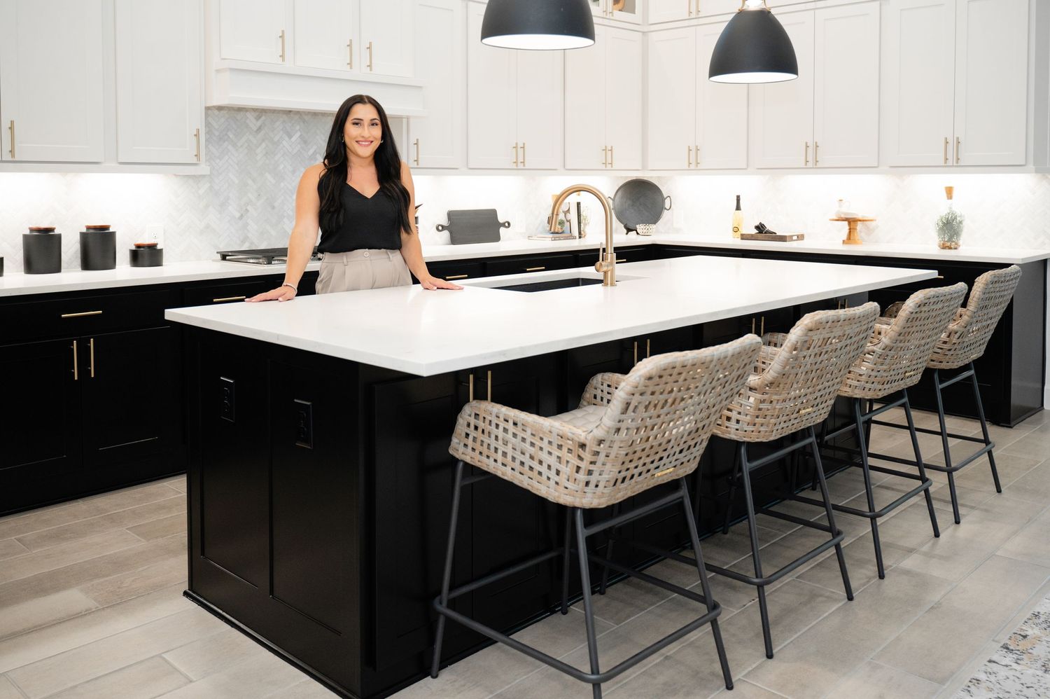 Modern white and black kitchen with upholstered bar chairs features pendant lighting and sleek minimalist design.