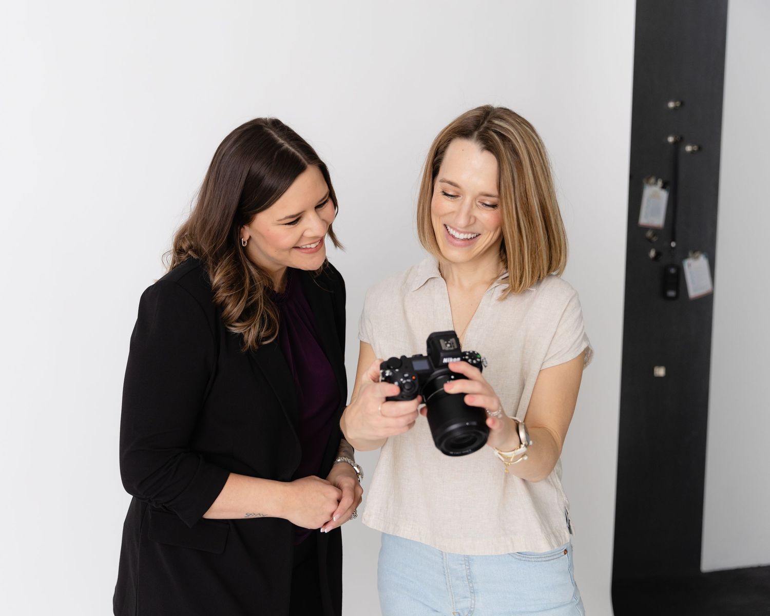 Two people laughing and sharing a joyful moment together while looking at a camera in a white studio setting.