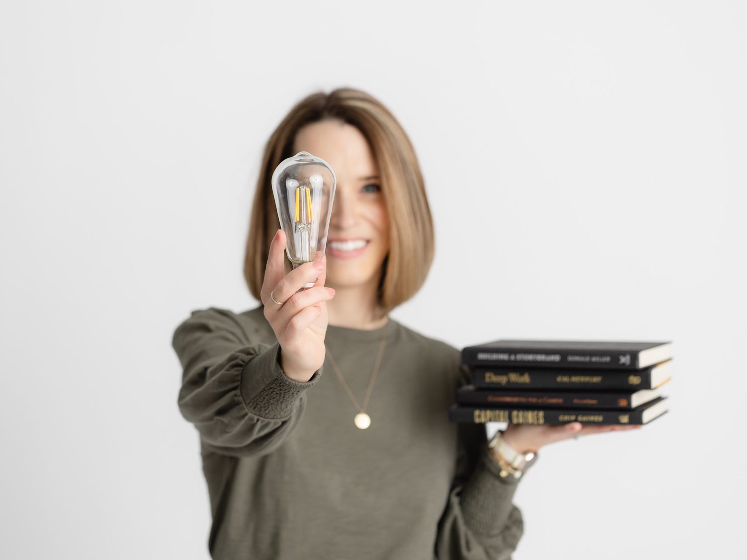 Professional holding a stack of books and money while smiling in a casual olive green top.