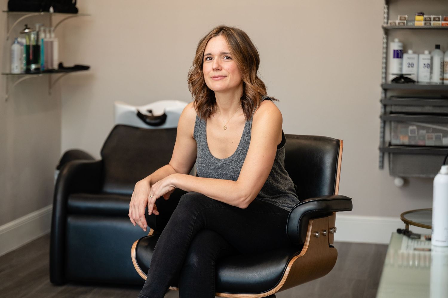 A person in a black sleeveless top sits on a leather chair in what appears to be a salon or spa setting.
