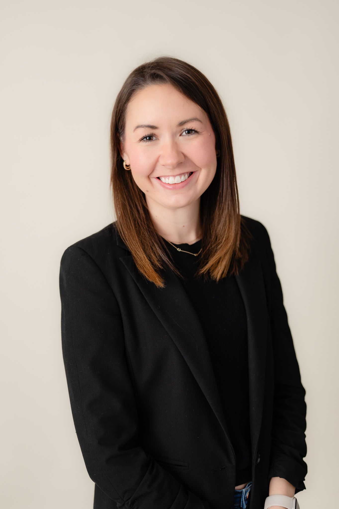 Professional headshot of someone in a black blazer against a light neutral background smiling warmly at the camera.