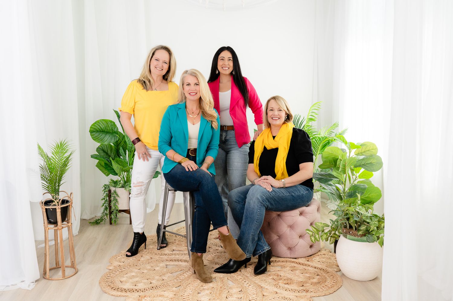 Professional business colleagues sit together on a white couch in a bright modern office with plants.