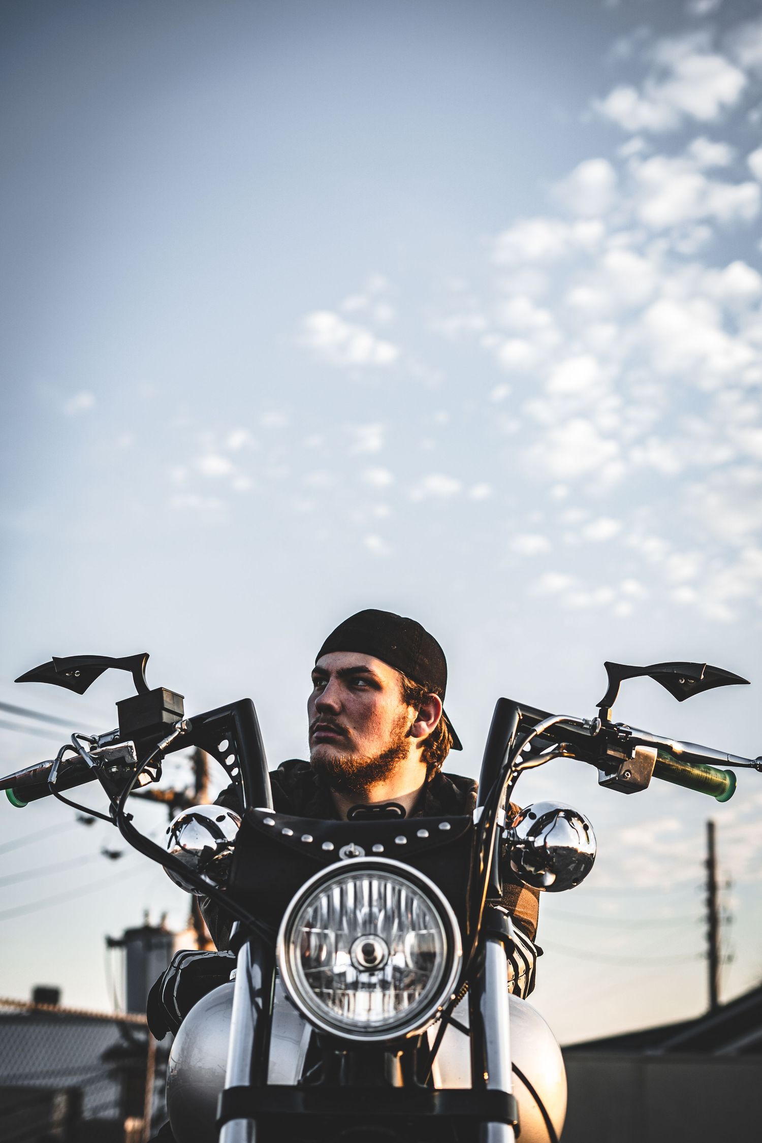 A motorcycle rider sits on a custom bike against a cloudy sky in three similar artistic shots at sunset.