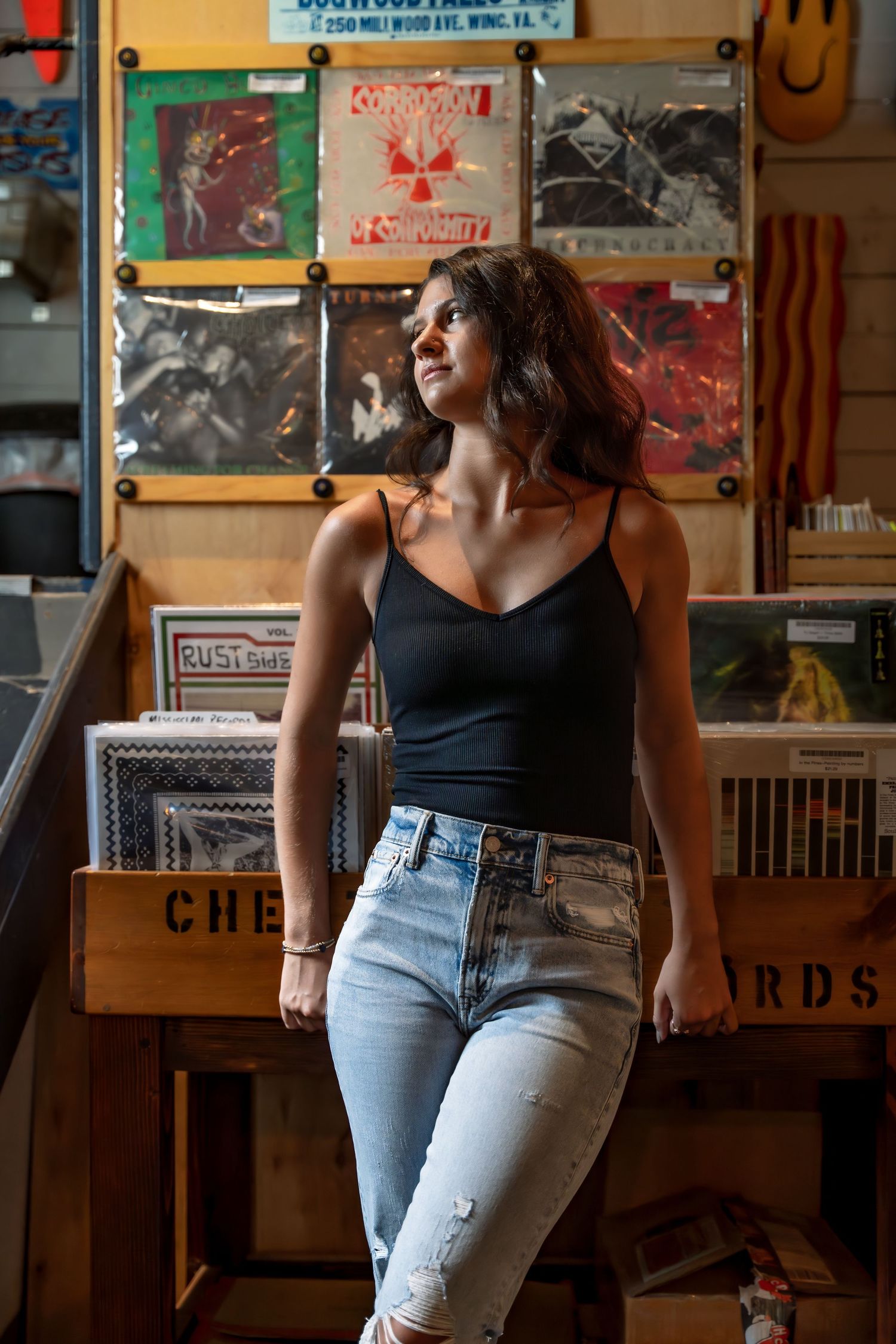 A person in a black tank top and light jeans browses through vinyl records at a music store.