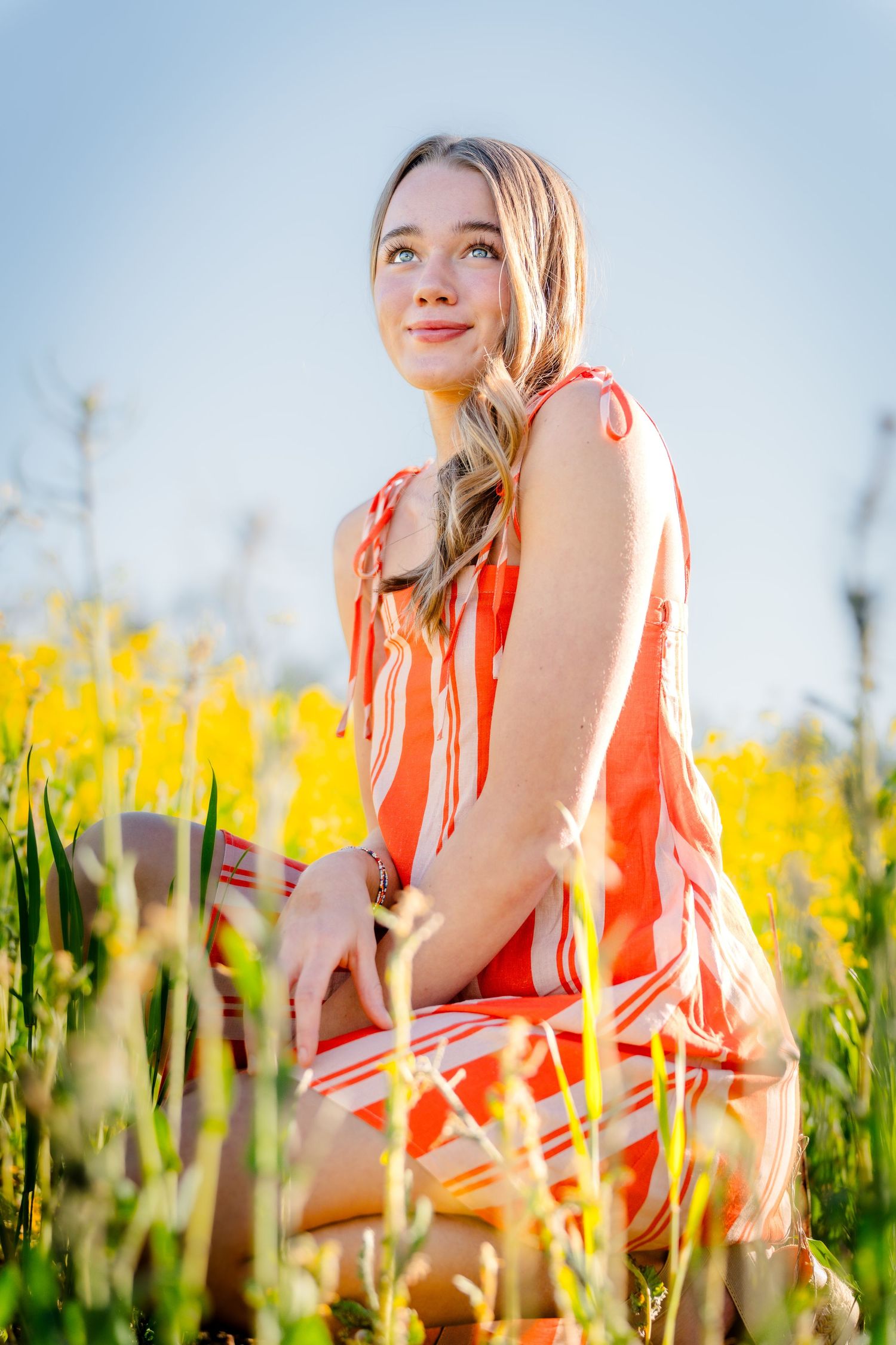A person in a coral dress poses gracefully among vibrant yellow wildflowers in a sunny meadow.