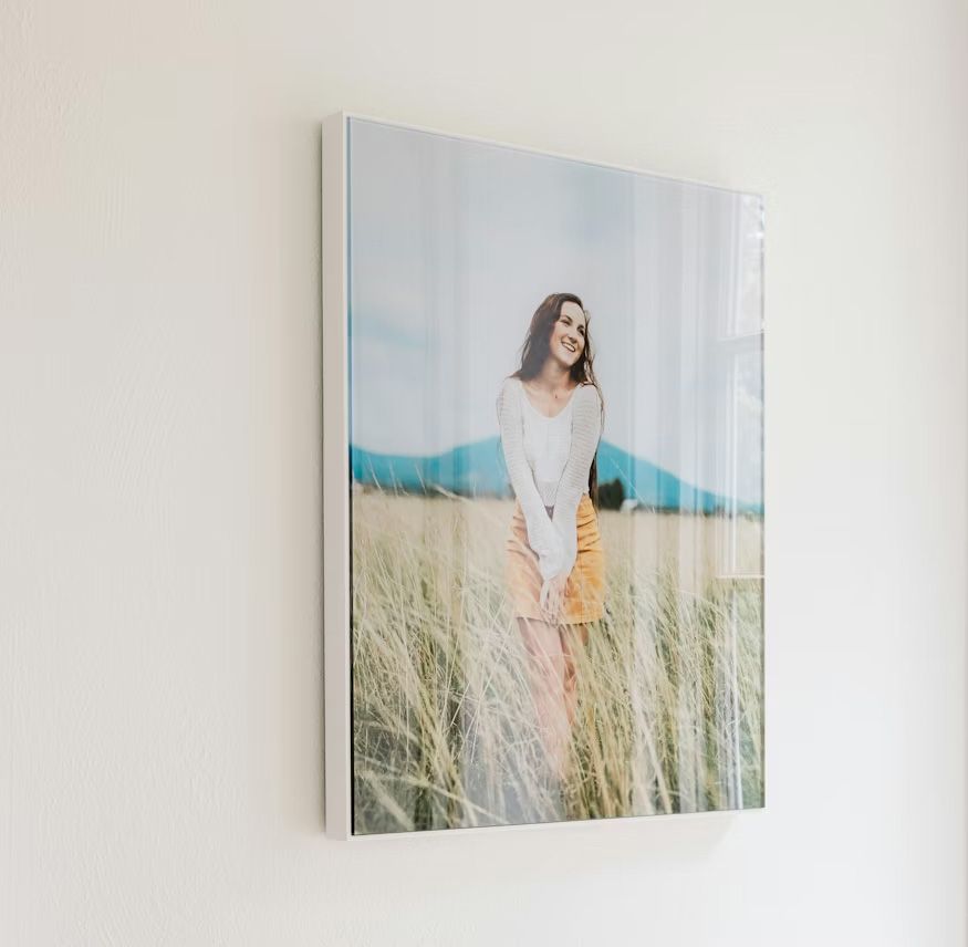 Three canvas prints of a woman in a white dress standing in a field of tall grass displayed on a white wall.