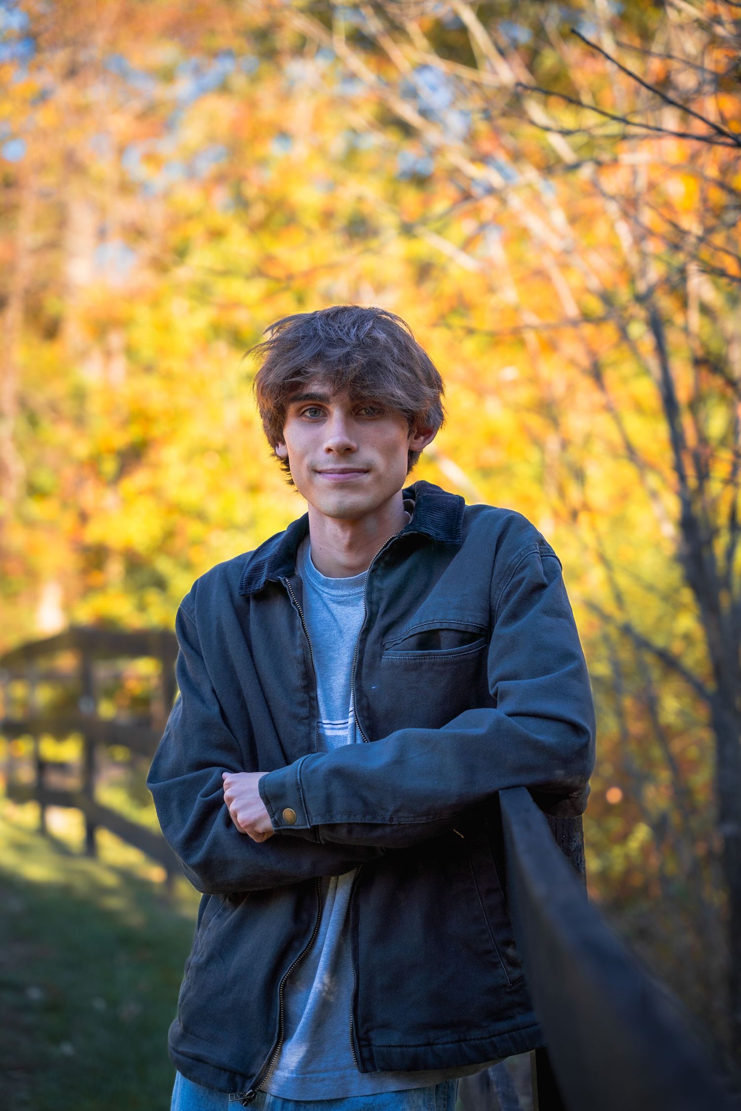 A person in a black jacket poses against vibrant autumn foliage with golden yellow leaves in the background.