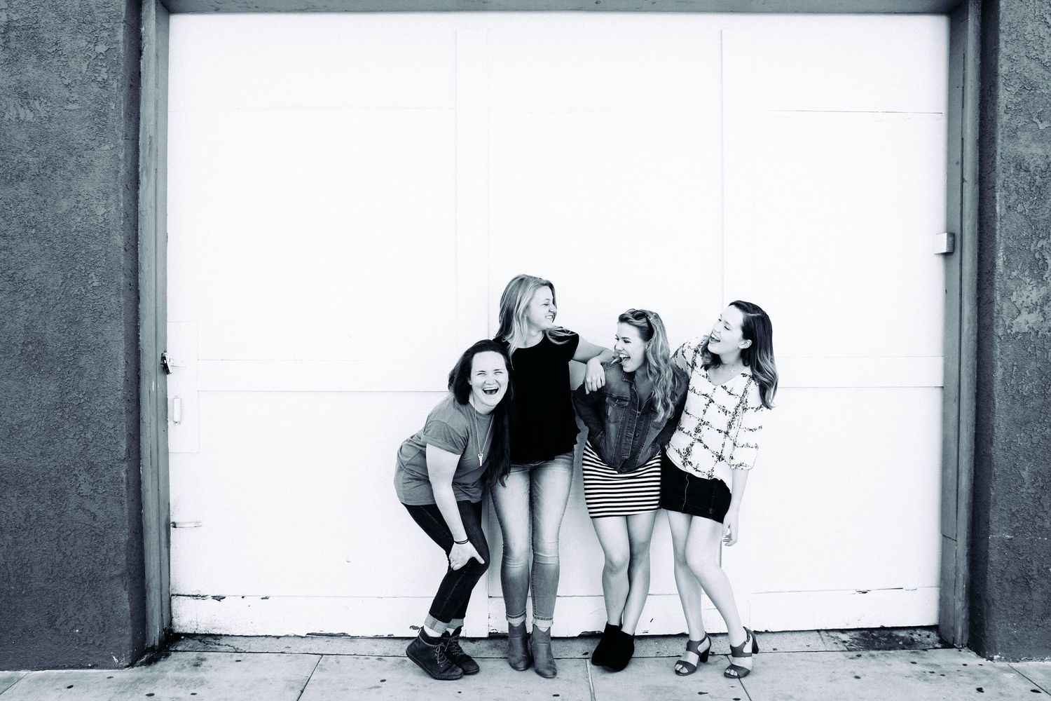 Black and white photo series showing a group of girls laughing together against a white wall.