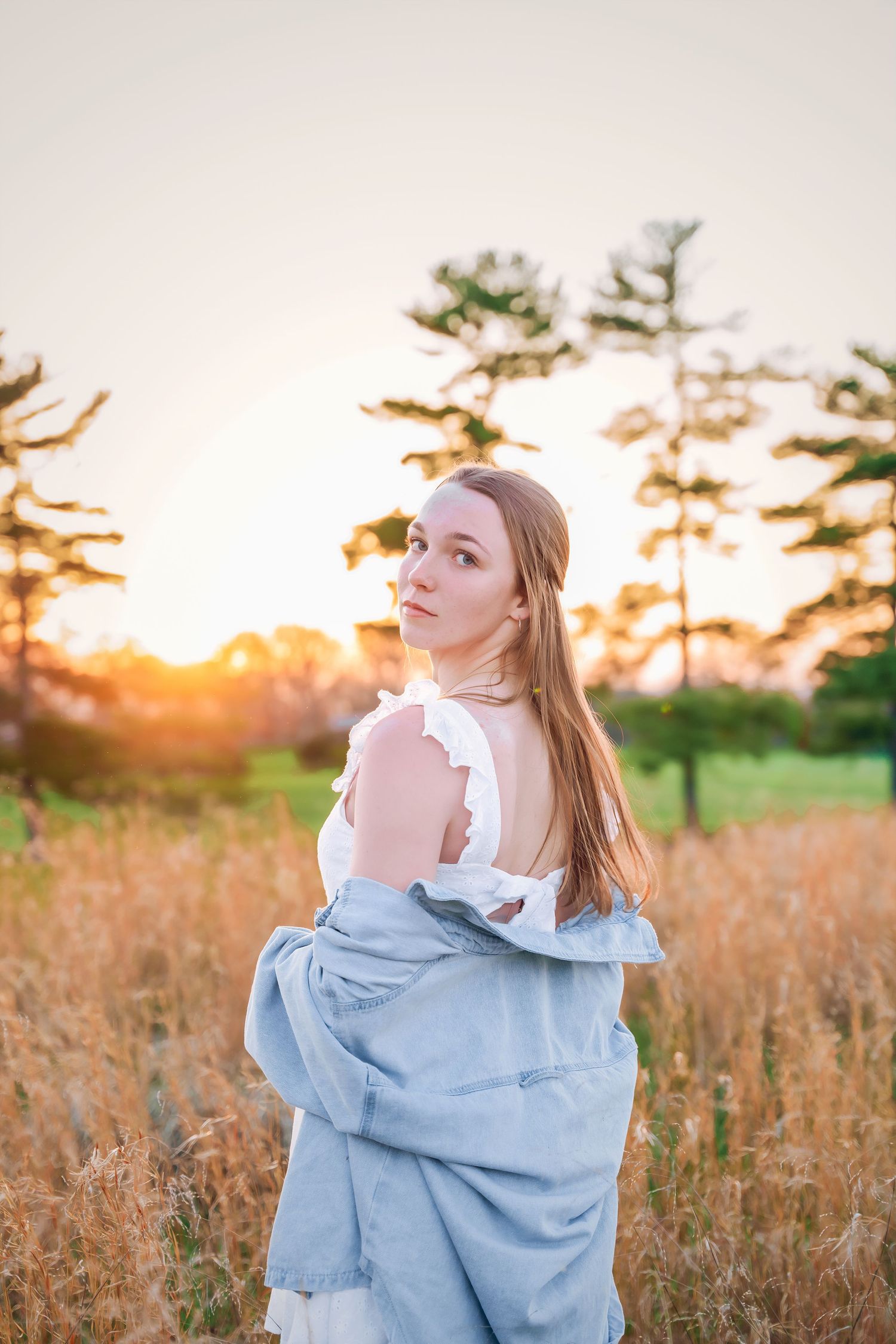 Dreamy sunset portrait with golden light filtering through pine trees.