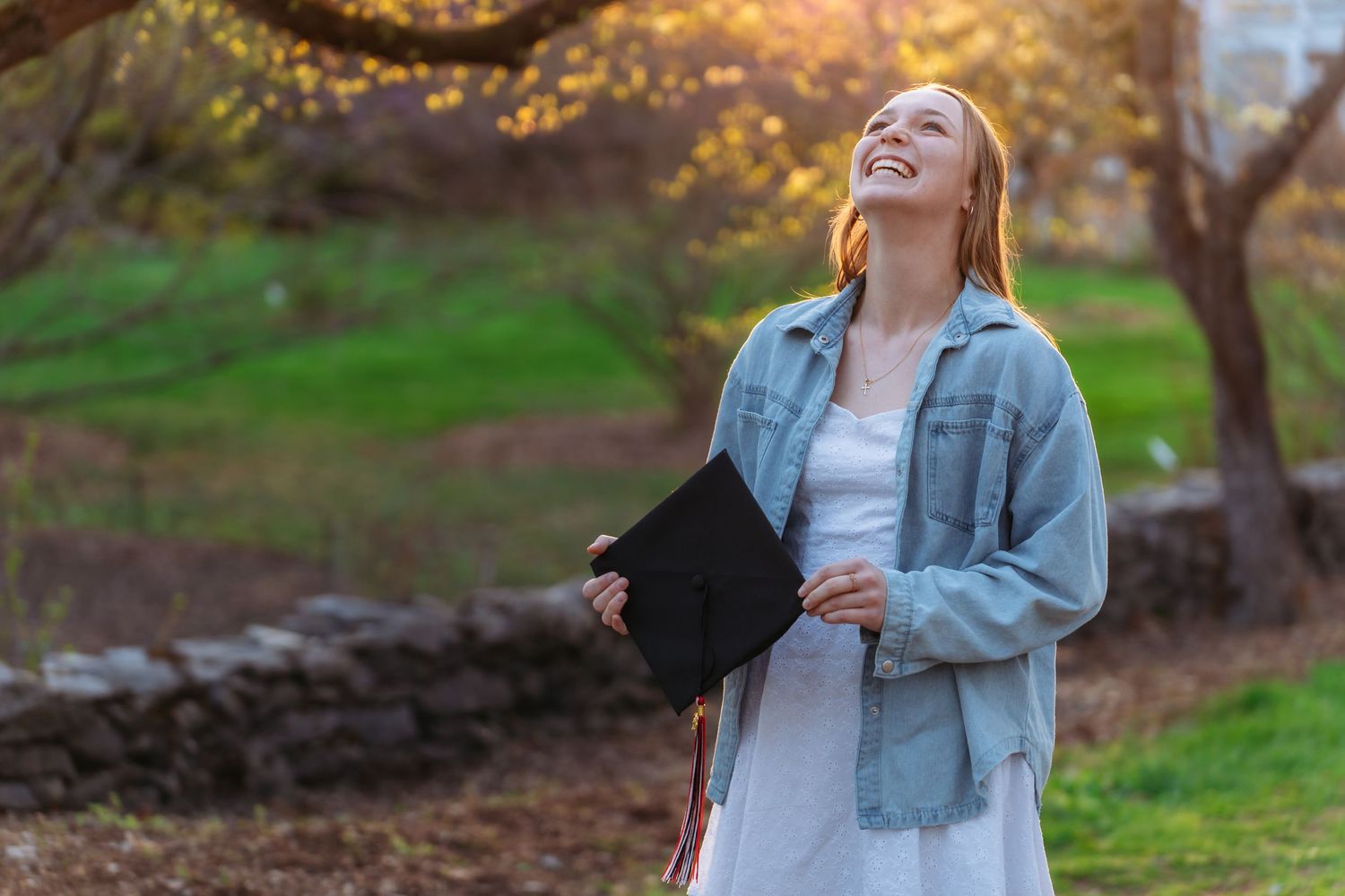 A joyful person in a denim jacket stands outdoors in a natural setting during golden hour lighting.