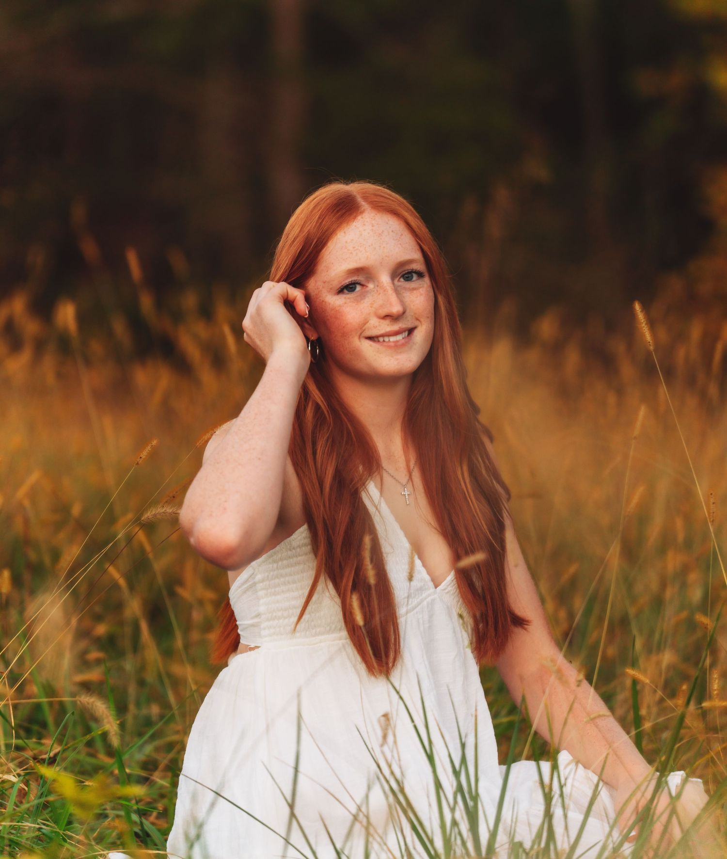 A woman in a white dress poses gracefully in a sunlit meadow of tall grass during golden hour.