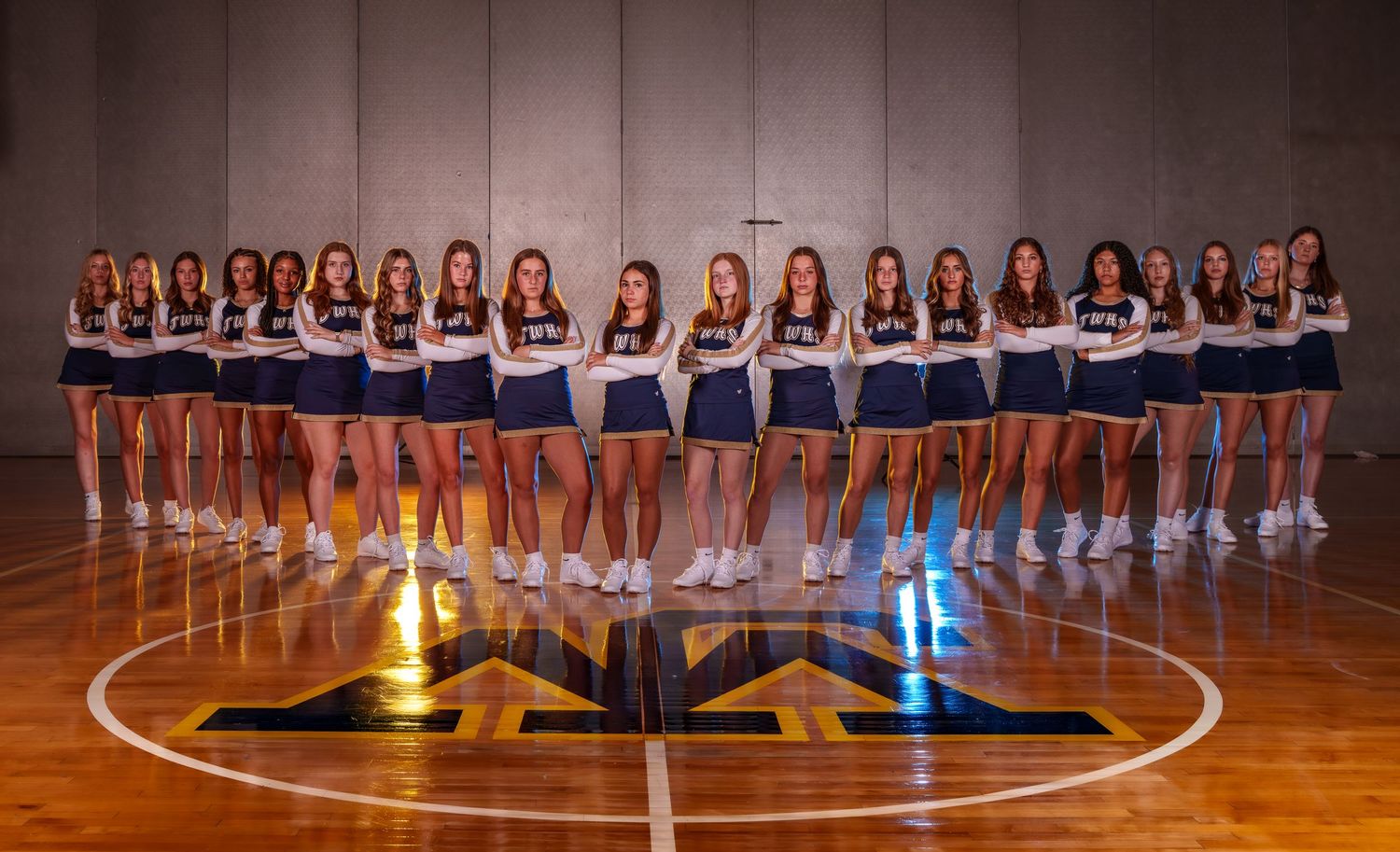 Basketball team members stand in formation on a glossy wooden court with dramatic lighting and reflections.