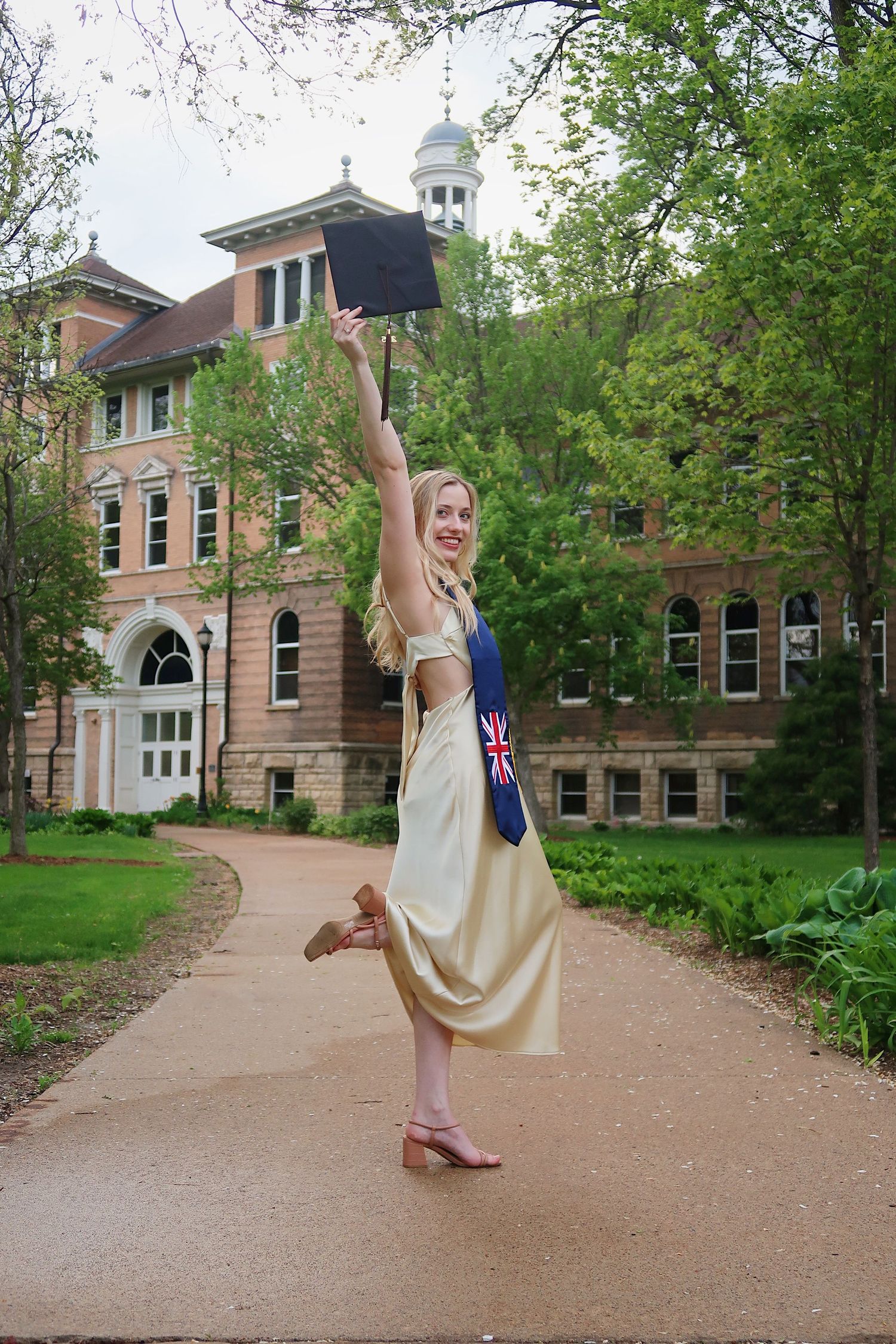 Graduate raising her cap above her head in front of her university for photoshoot
