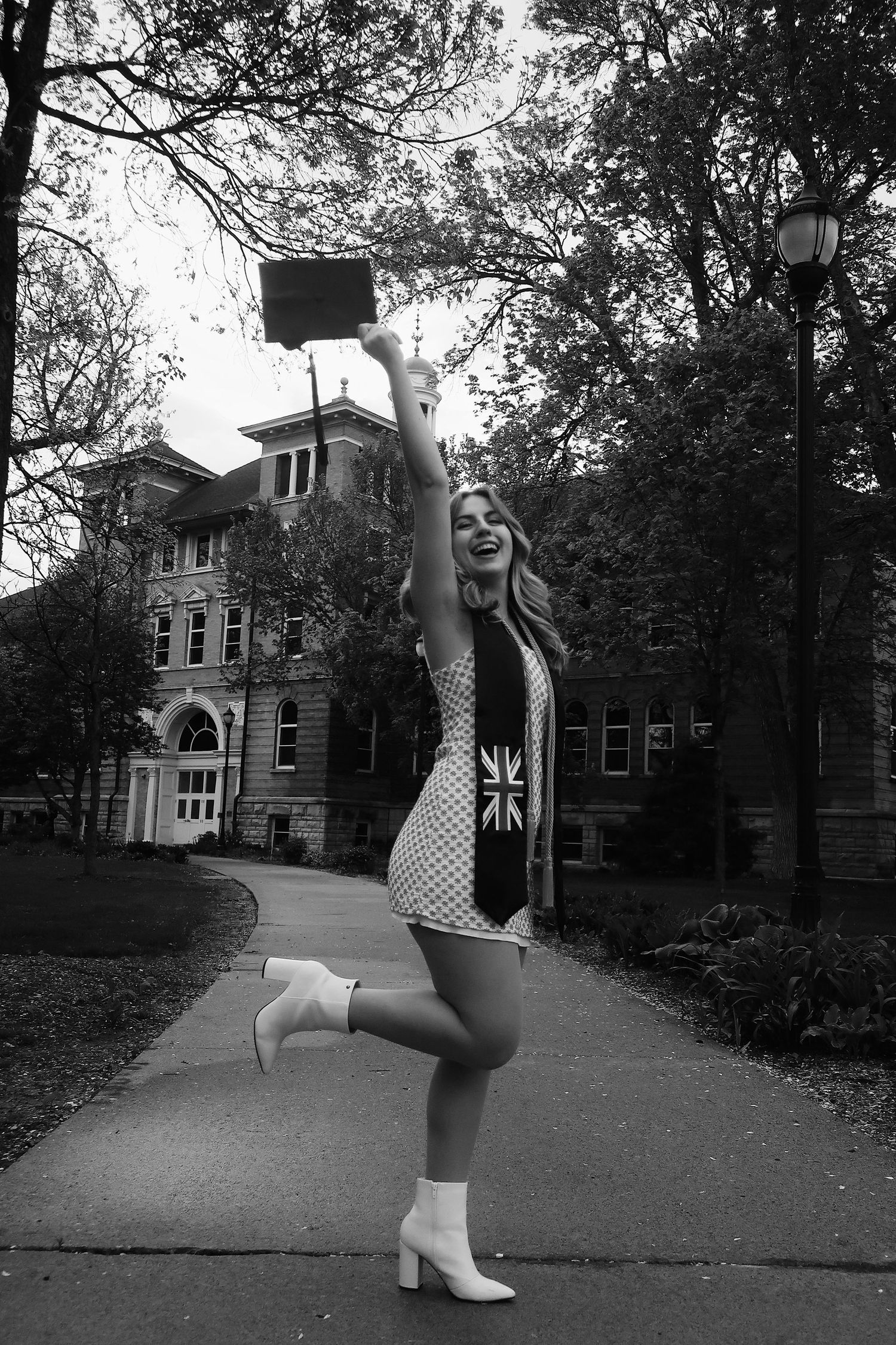 Graduate raising her cap above her head in front of her university for photoshoot, black and white