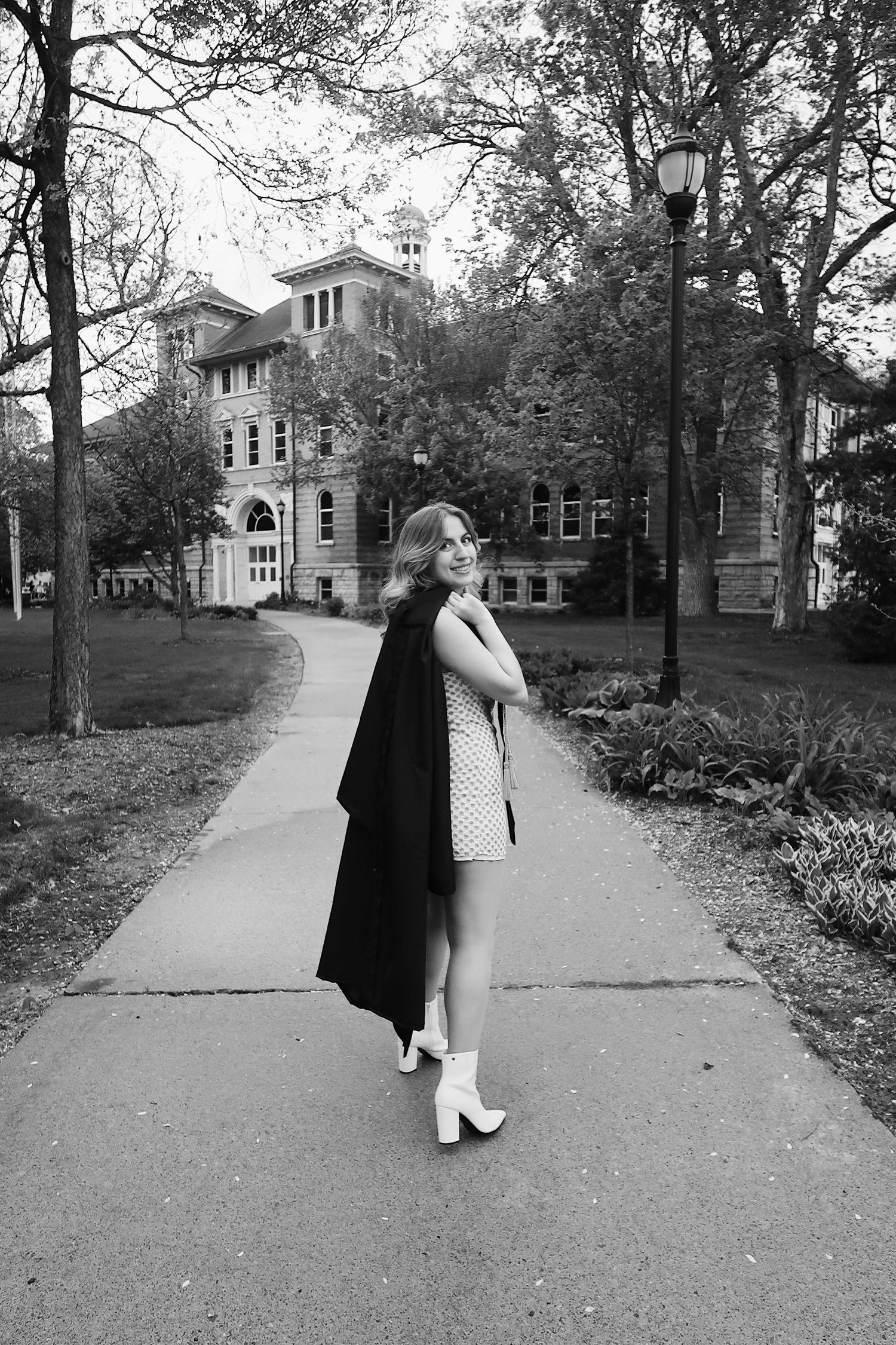 Graduate hanging her gown over her shoulder in front of her university for photoshoot