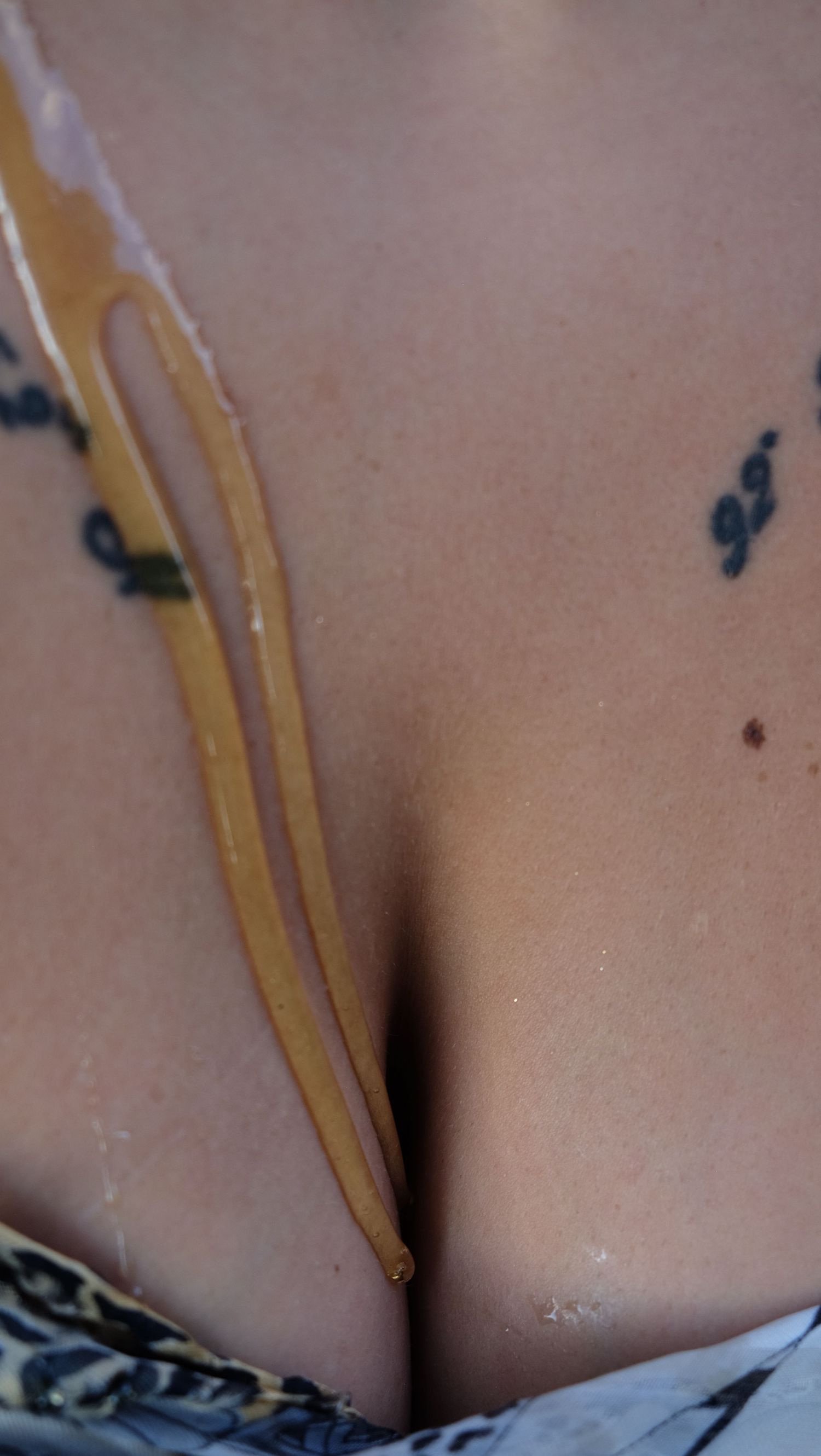 Close-up of a tattooed chest with golden honey dripping down the center, with a leopard print top below.