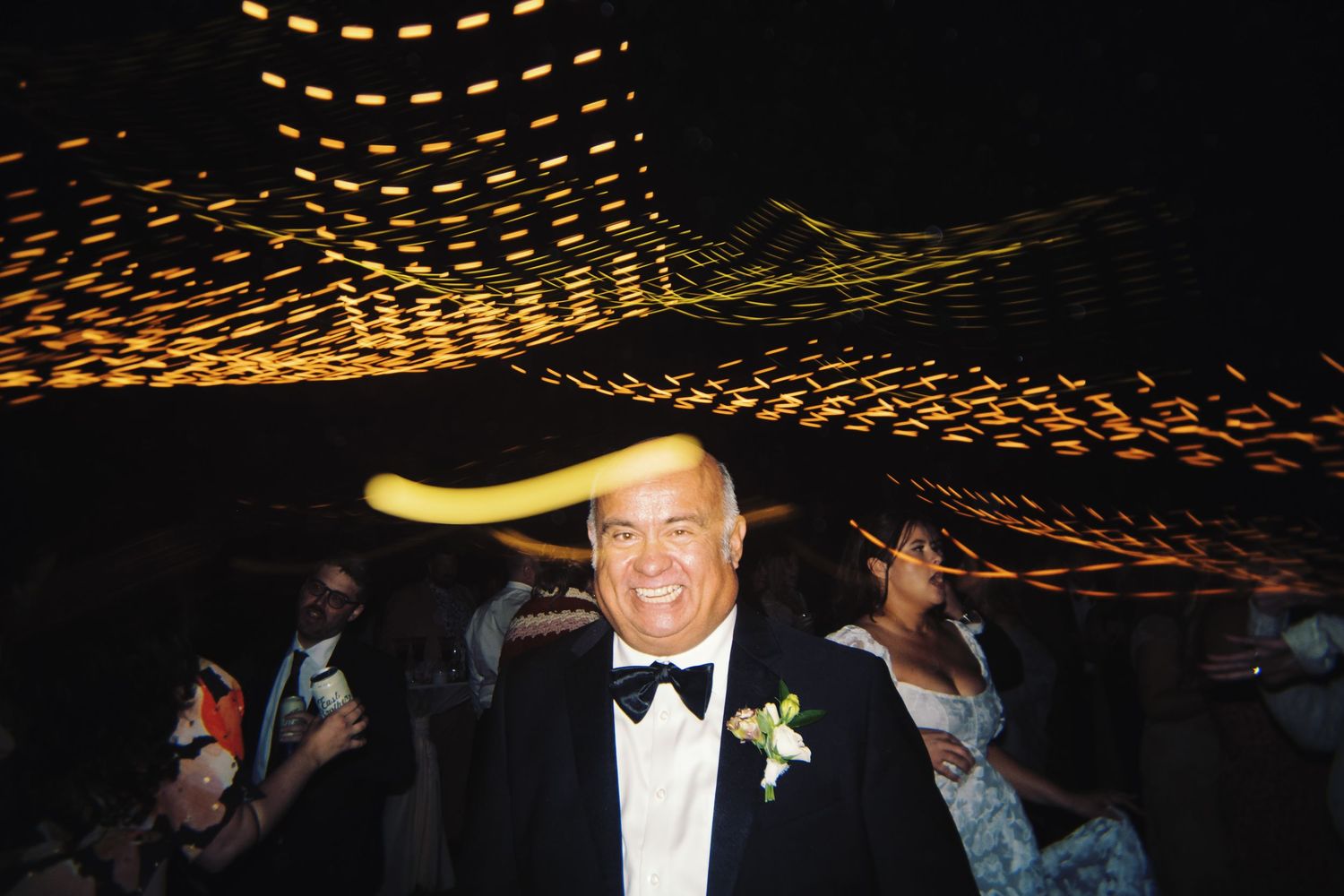 Smiling man in tuxedo with a yellow banana on his head at a fun wedding reception.