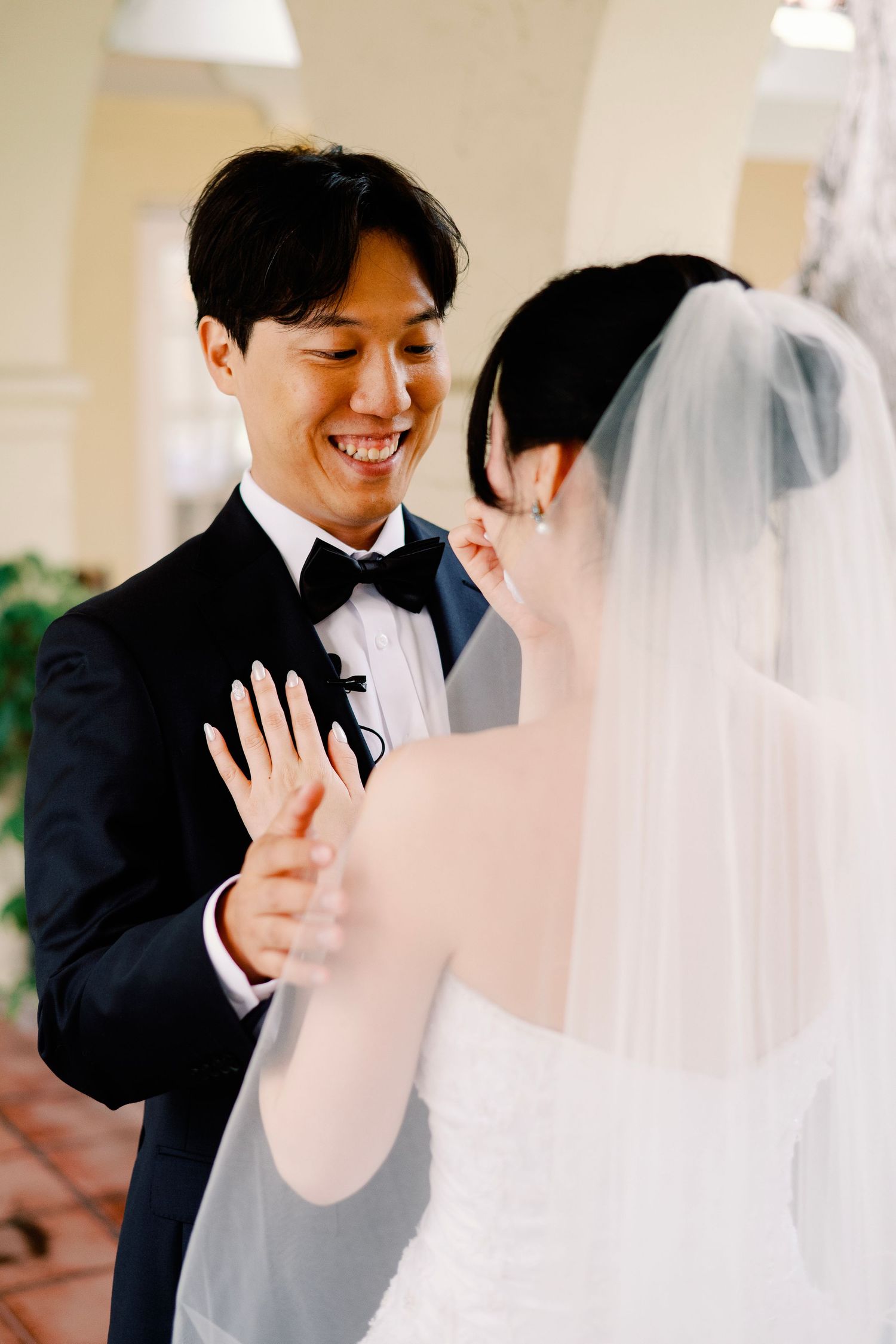 Groom laughing happily while holding bride's hand during wedding first look.