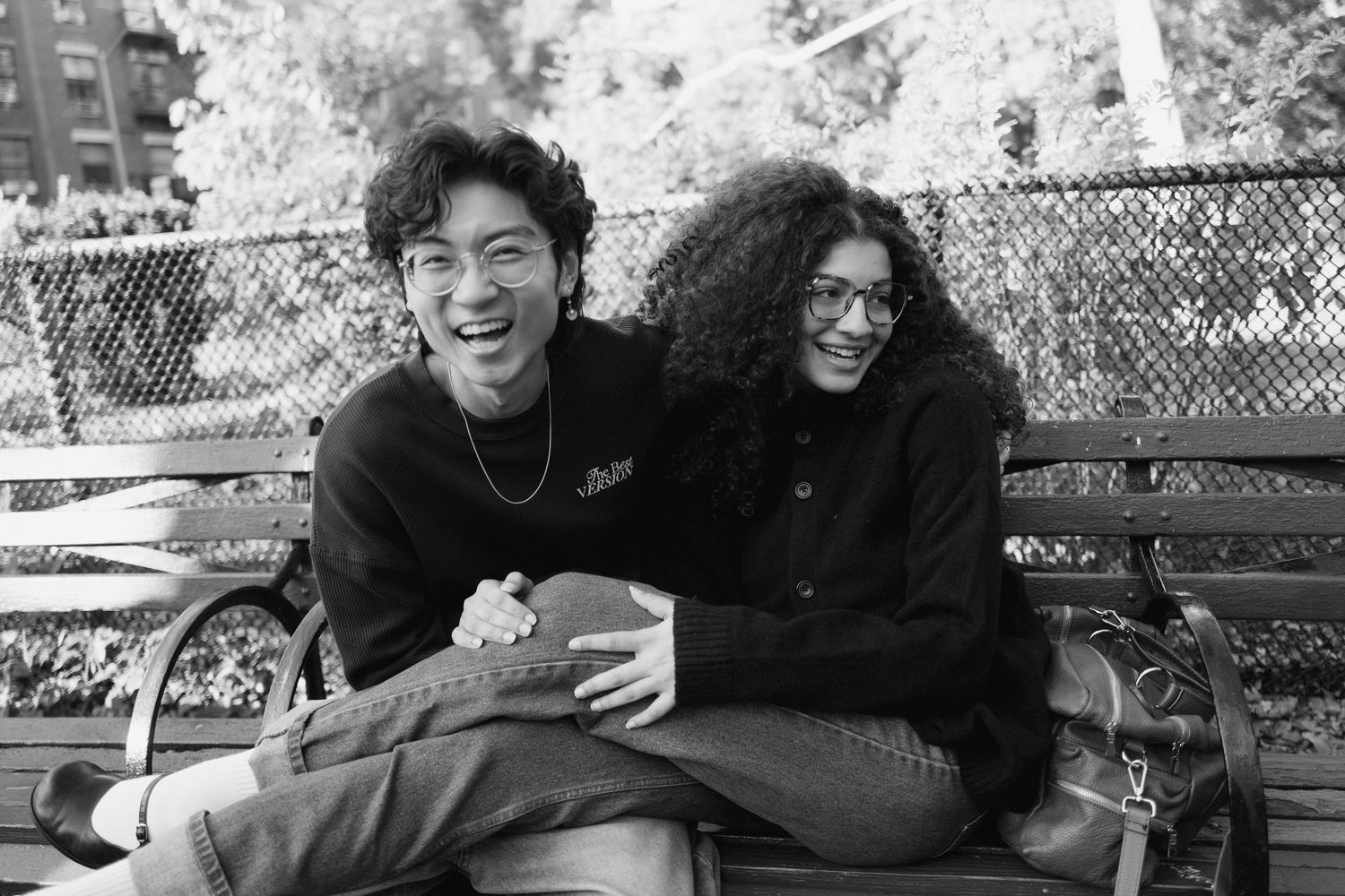 Laughing couple sitting closely together on a park bench, sharing a joyful moment in black and white.